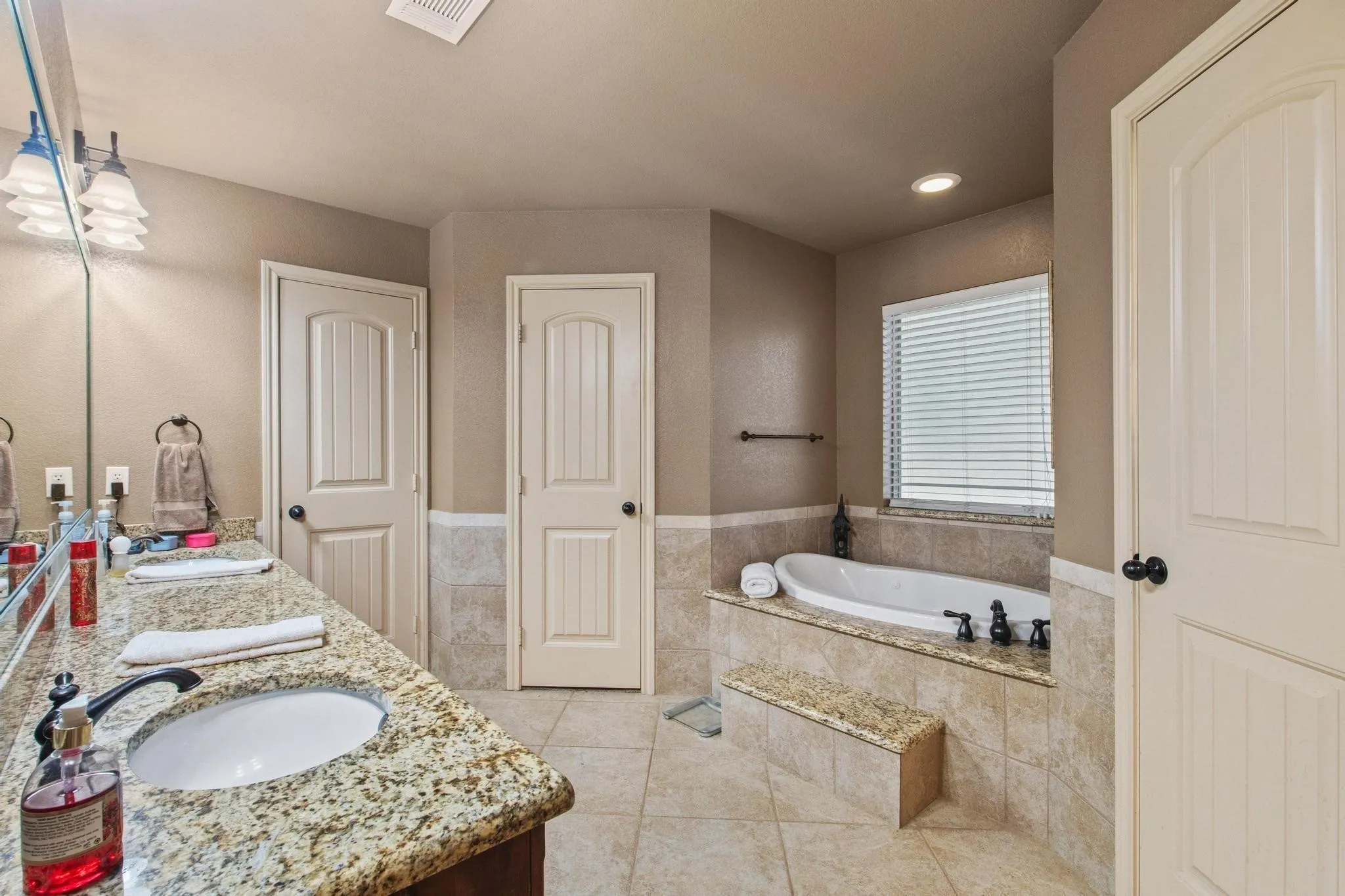 Spa-inspired primary bathroom featuring dual vanities with granite countertops, an undermount sink, and polished chrome fixtures