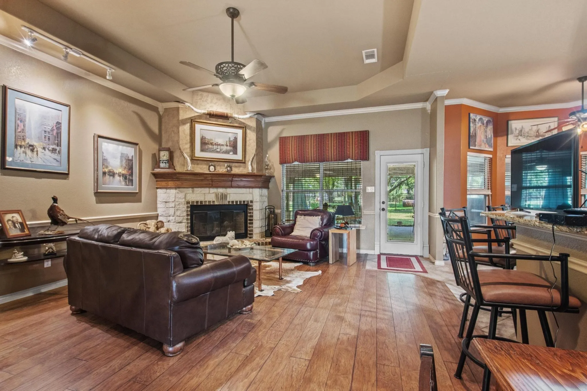 Wood-finish flooring throughout, stone-faced fireplace with wood mantel, ceiling fan, track lighting, and a glass-paneled exterior door