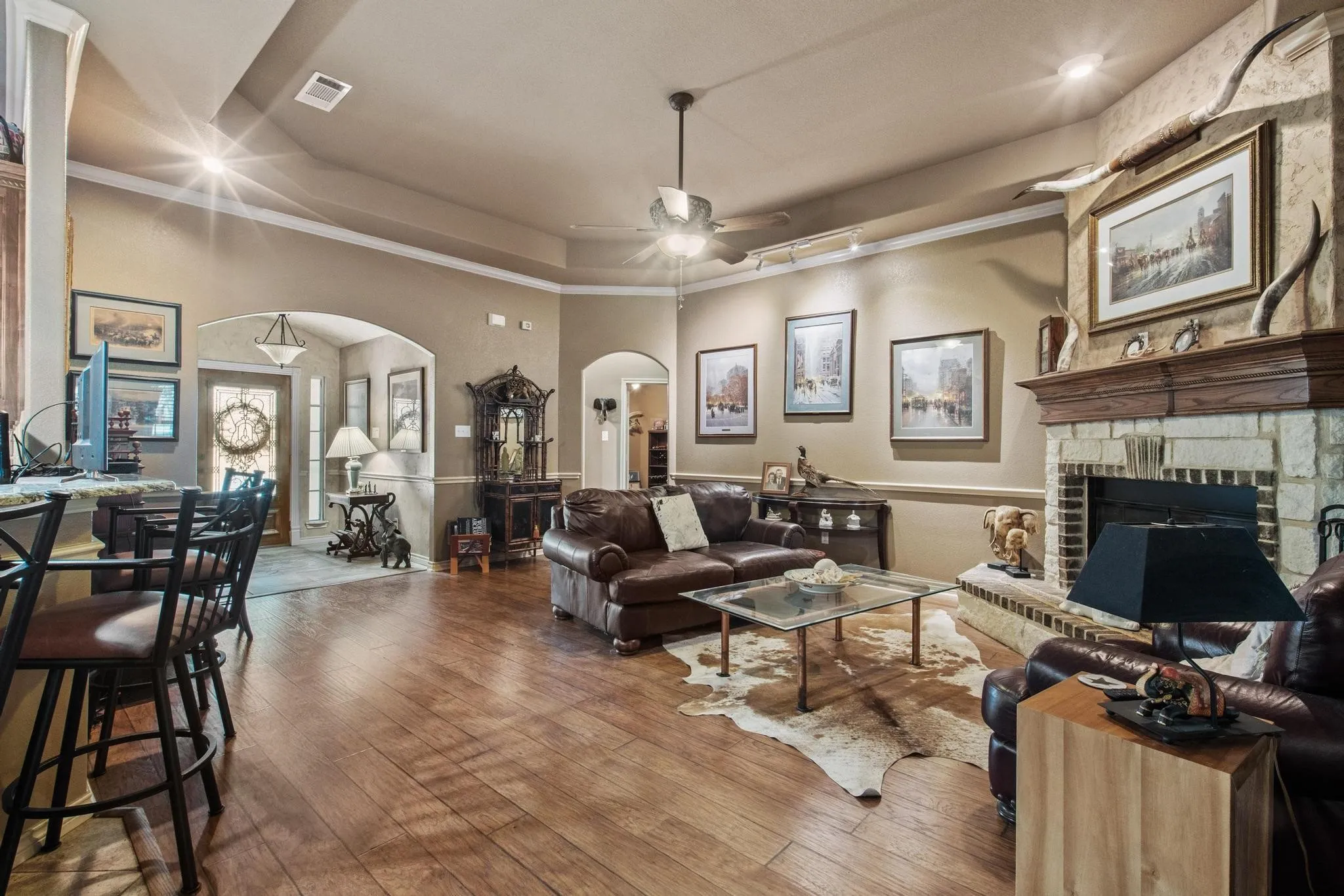 Spacious living area featuring wood-finish flooring, a stone fireplace with a substantial wood mantel, and crown molding