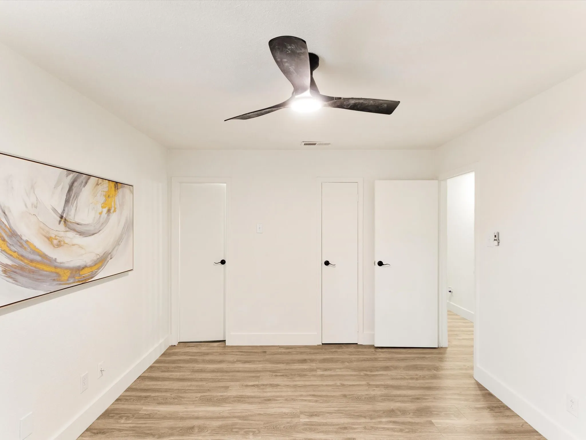 Wood-finish flooring, white walls, and a modern ceiling fan