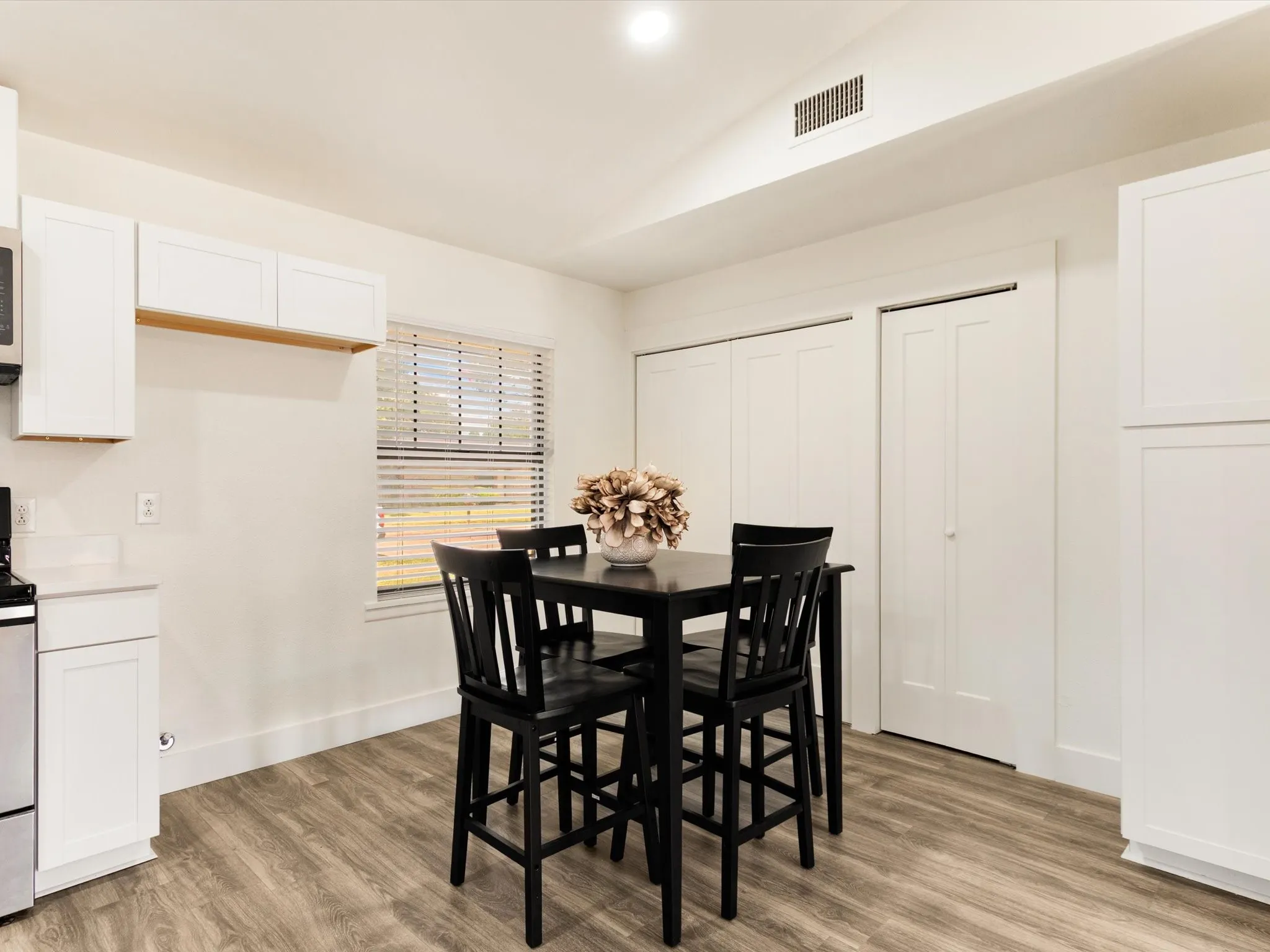 White cabinetry with an open shelf, stainless steel appliances, and a window with blinds