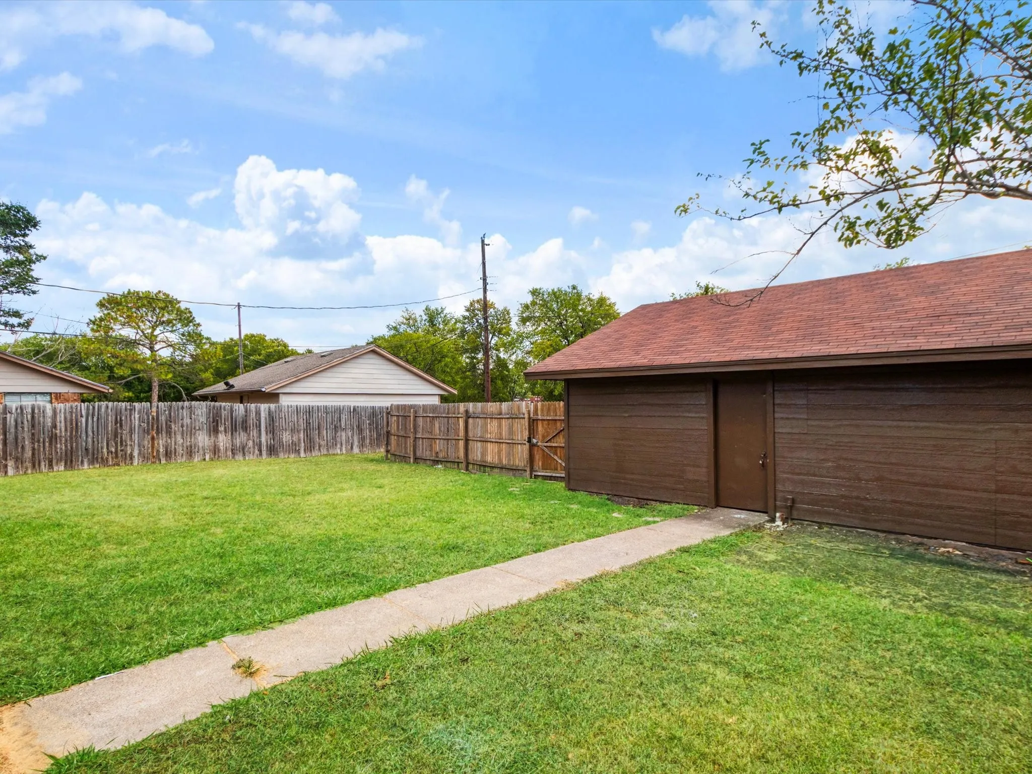 Expansive green lawn with a concrete pathway leading to a detached structure featuring brown siding and a brown shingle roof