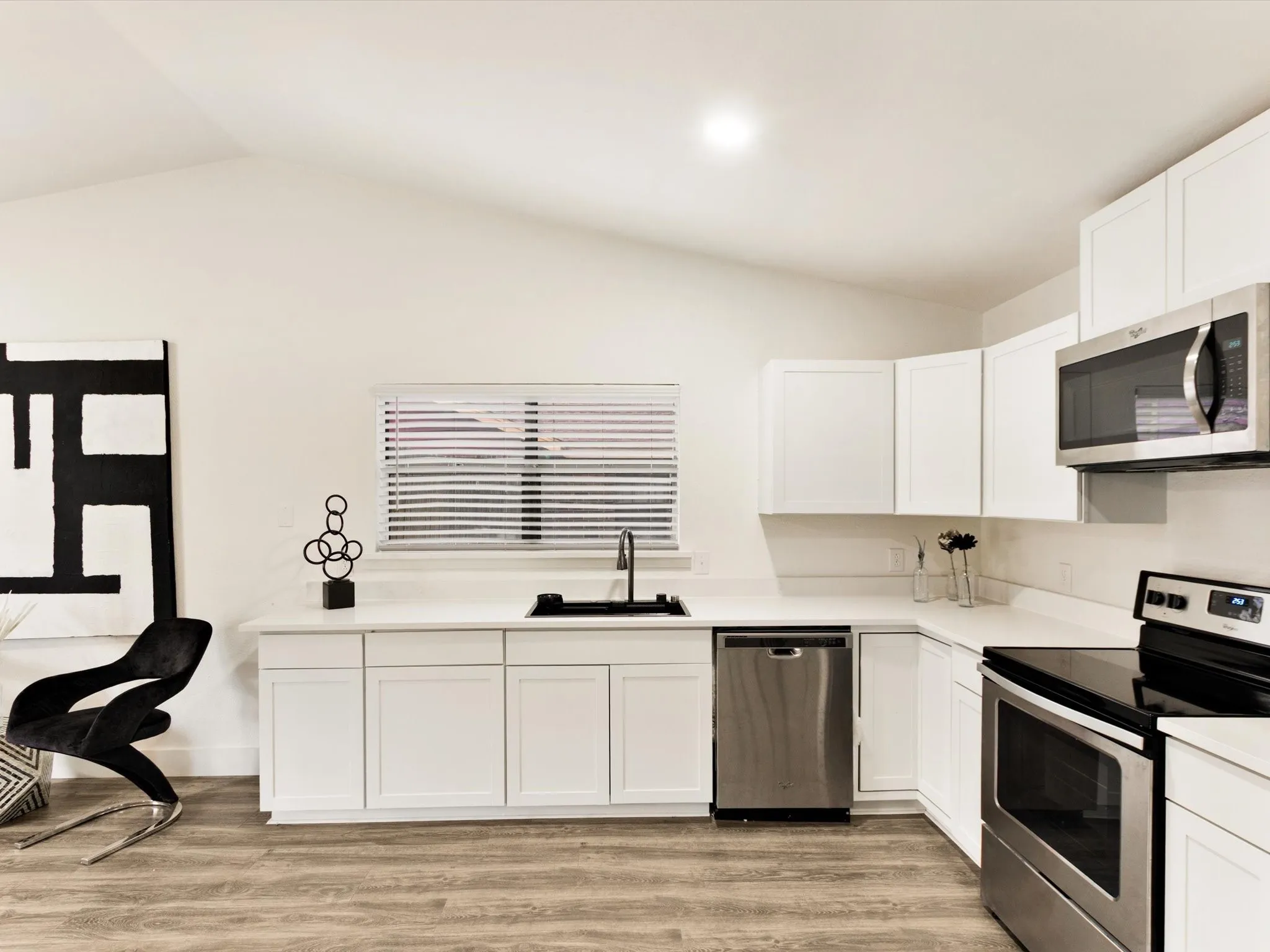 White cabinetry with stainless steel appliances, wood-finish flooring, and a black single-basin sink