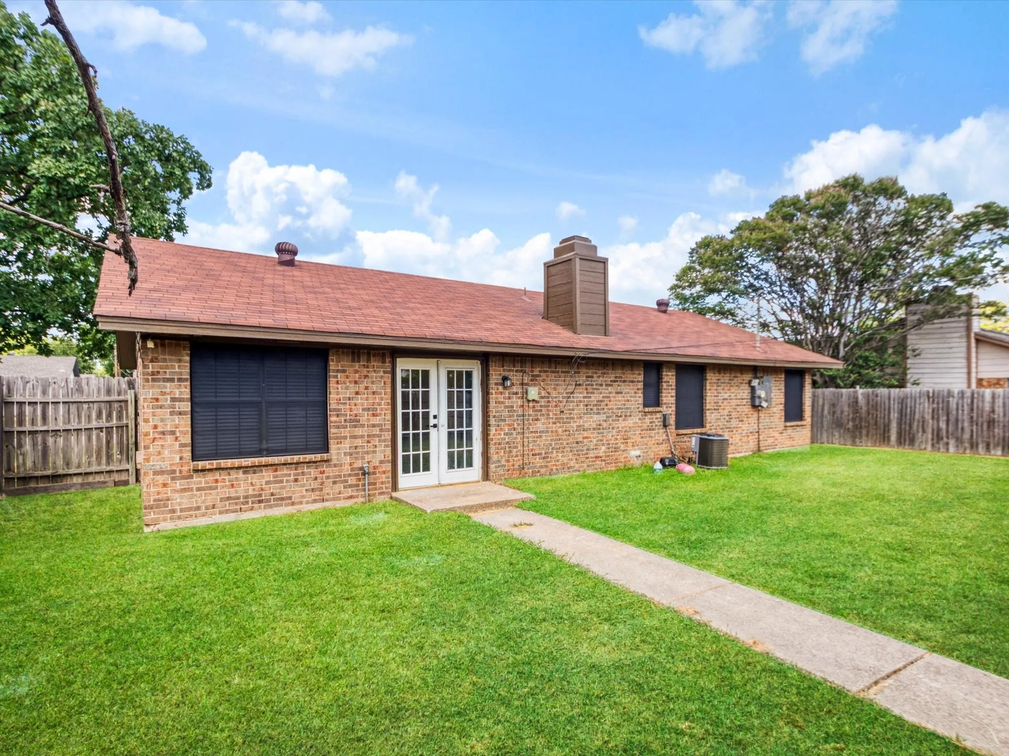 Brick exterior with a red shingle roof, double French doors, a concrete pathway, and a grassy yard