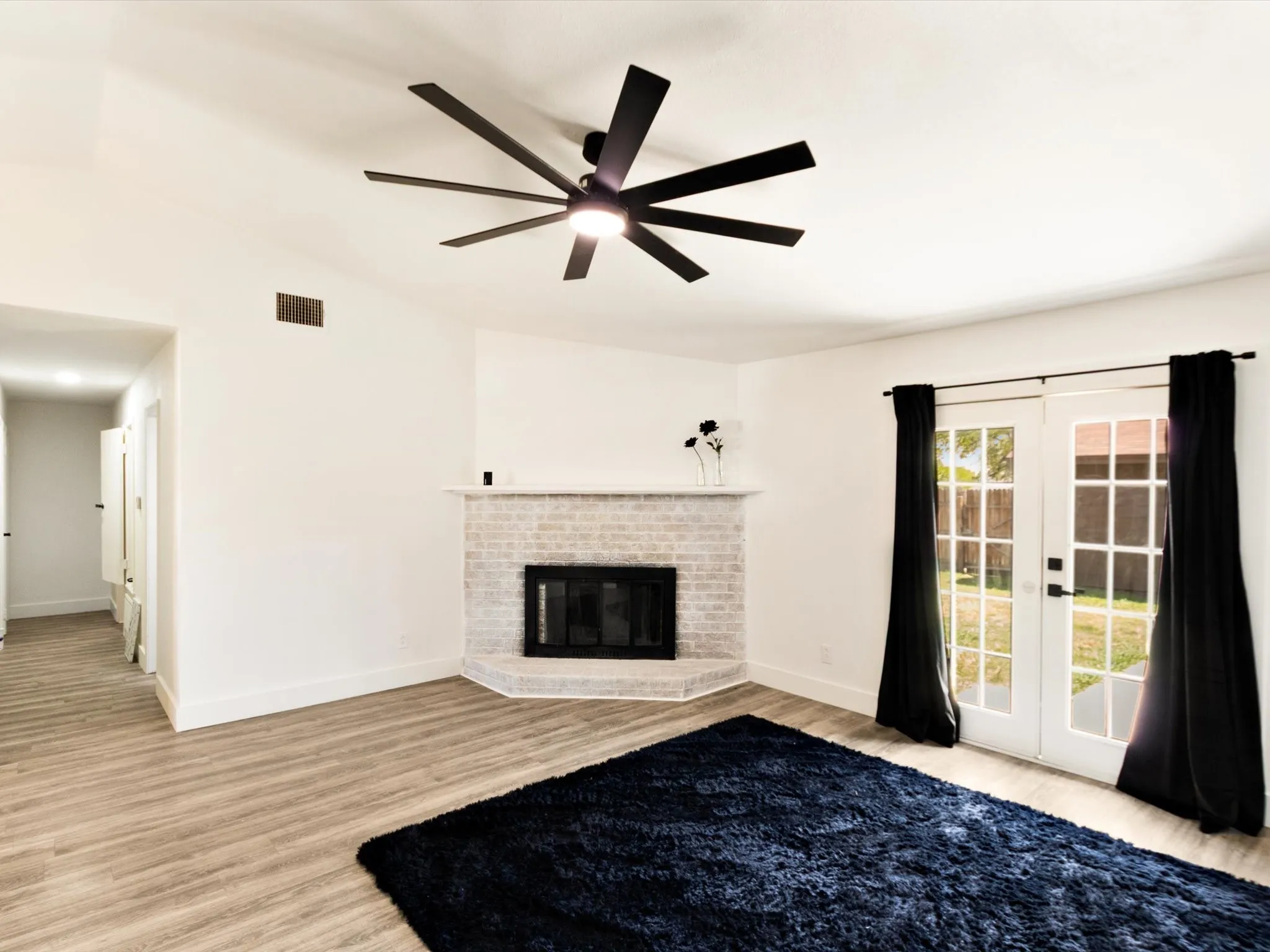 Living area with wood-finish flooring, a white brick fireplace, and a contemporary ceiling fan