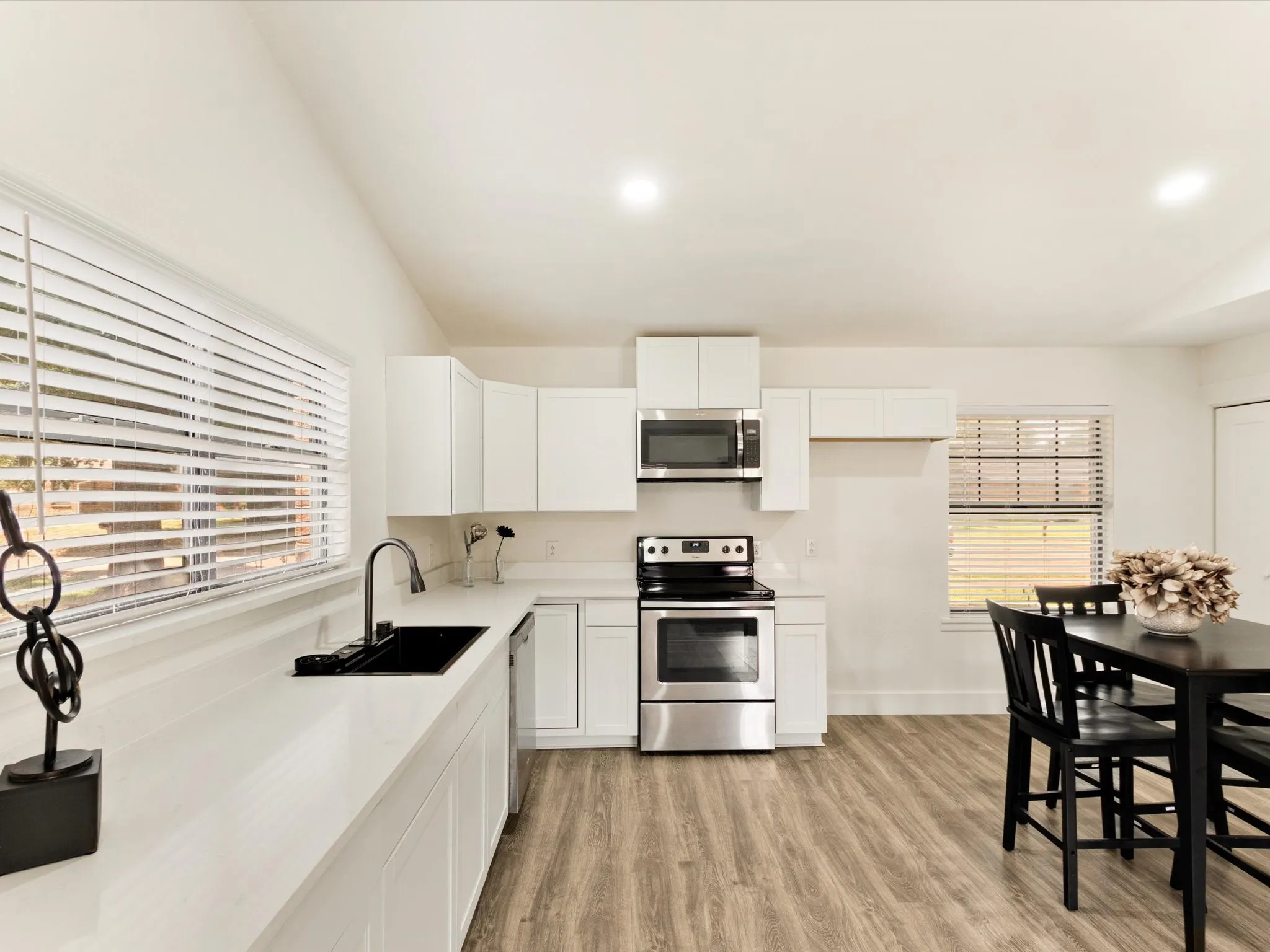 White cabinetry, stainless steel appliances, wood-finish flooring, recessed lighting, and a black sink with a gooseneck faucet