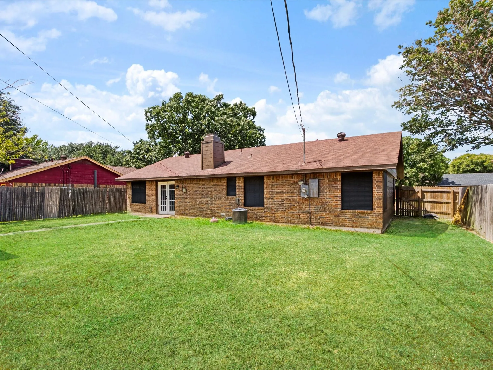 Expansive grassy backyard featuring a brick exterior, double French doors, and a wood privacy fence