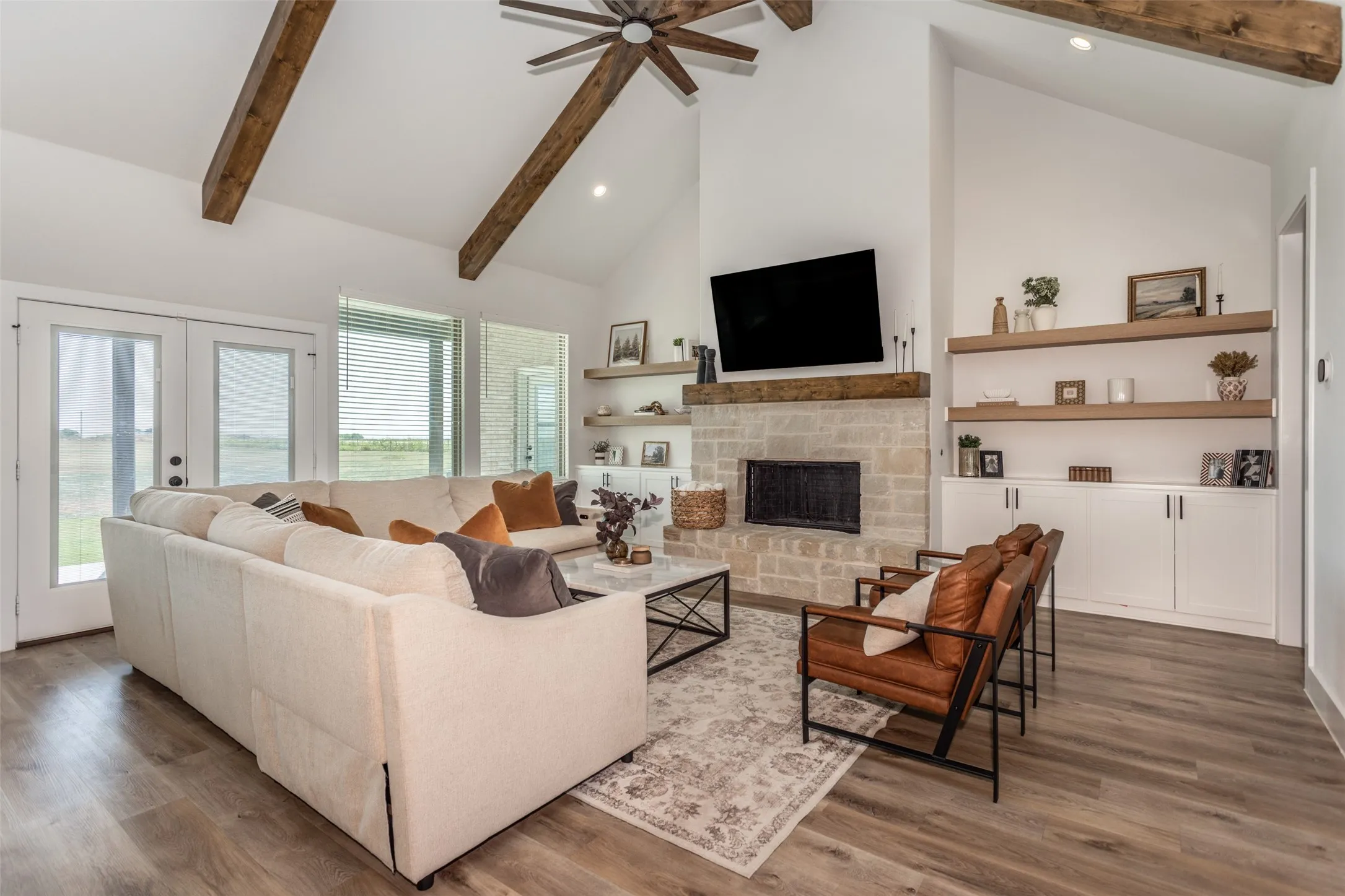 Vaulted ceiling with exposed wood beams, stone-clad fireplace with wood mantel, built-in shelving, built-in cabinetry, and wood-finish flooring