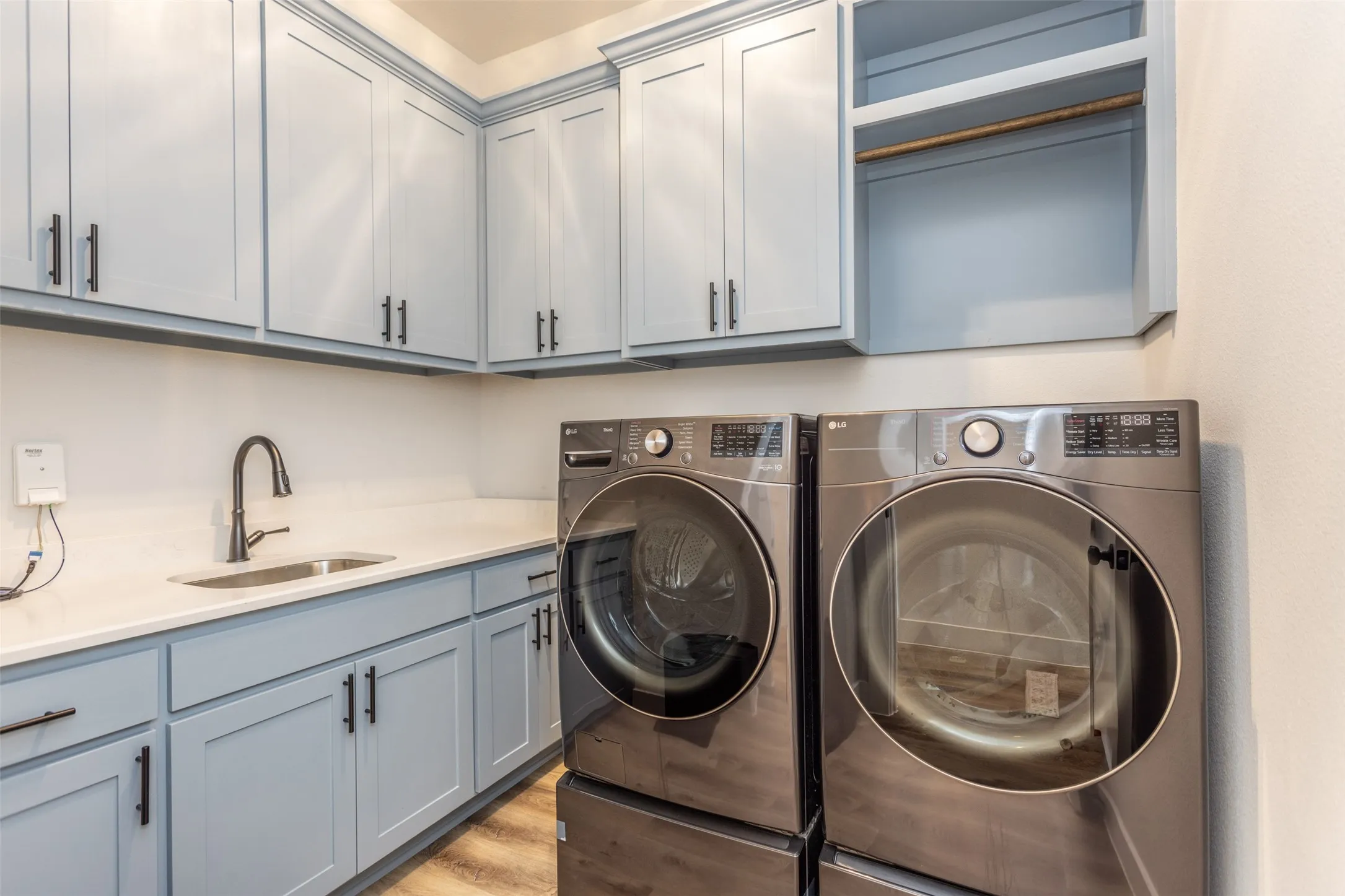 Light blue cabinetry with matte black hardware, white countertops, built-in sink with a gooseneck faucet, and wood-finish flooring