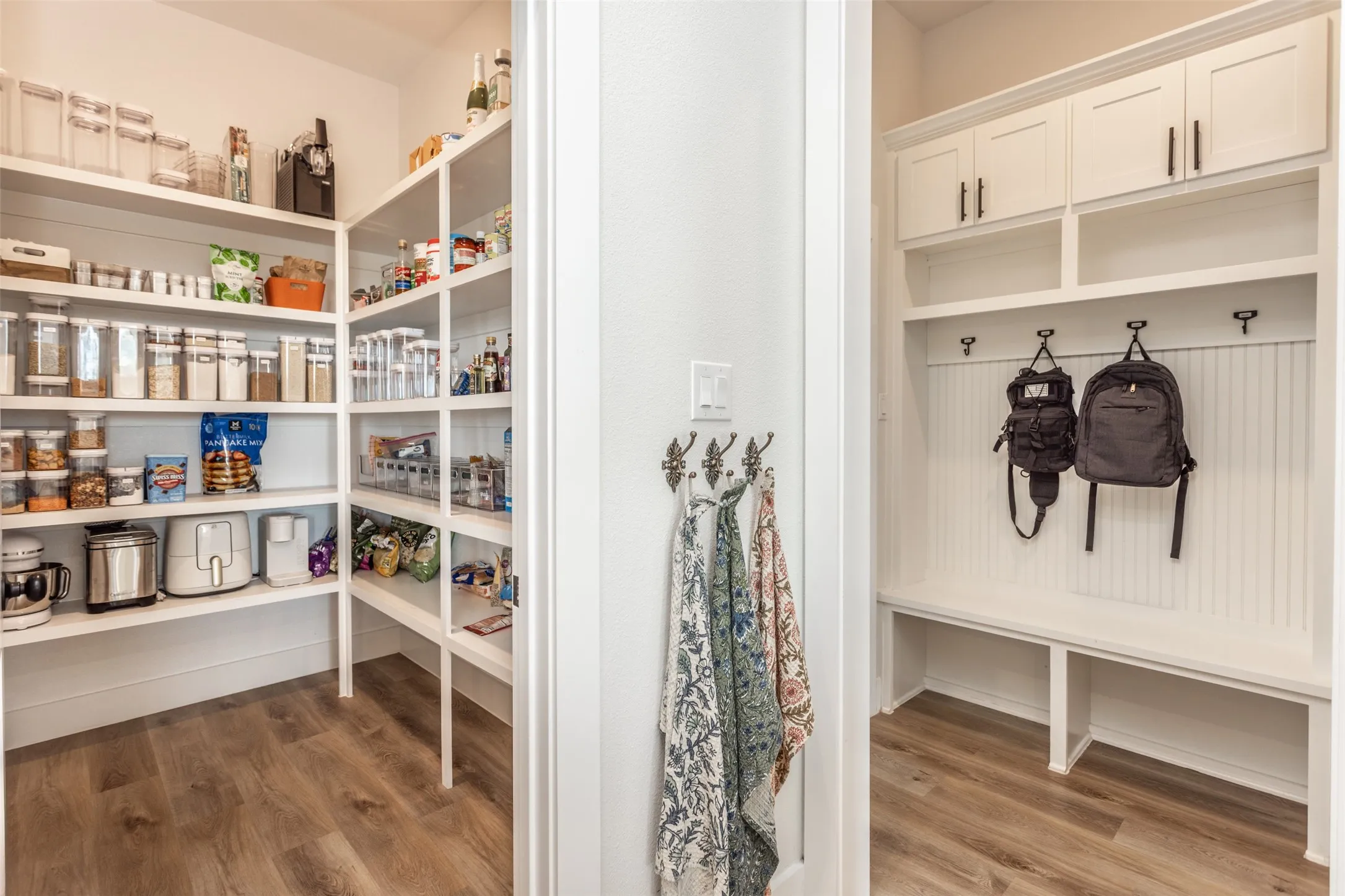 Dual-purpose storage spaces featuring custom white cabinetry with ample shelving for pantry organization and a dedicated mudroom with wall-mounted hooks, built-in benches, and upper storage