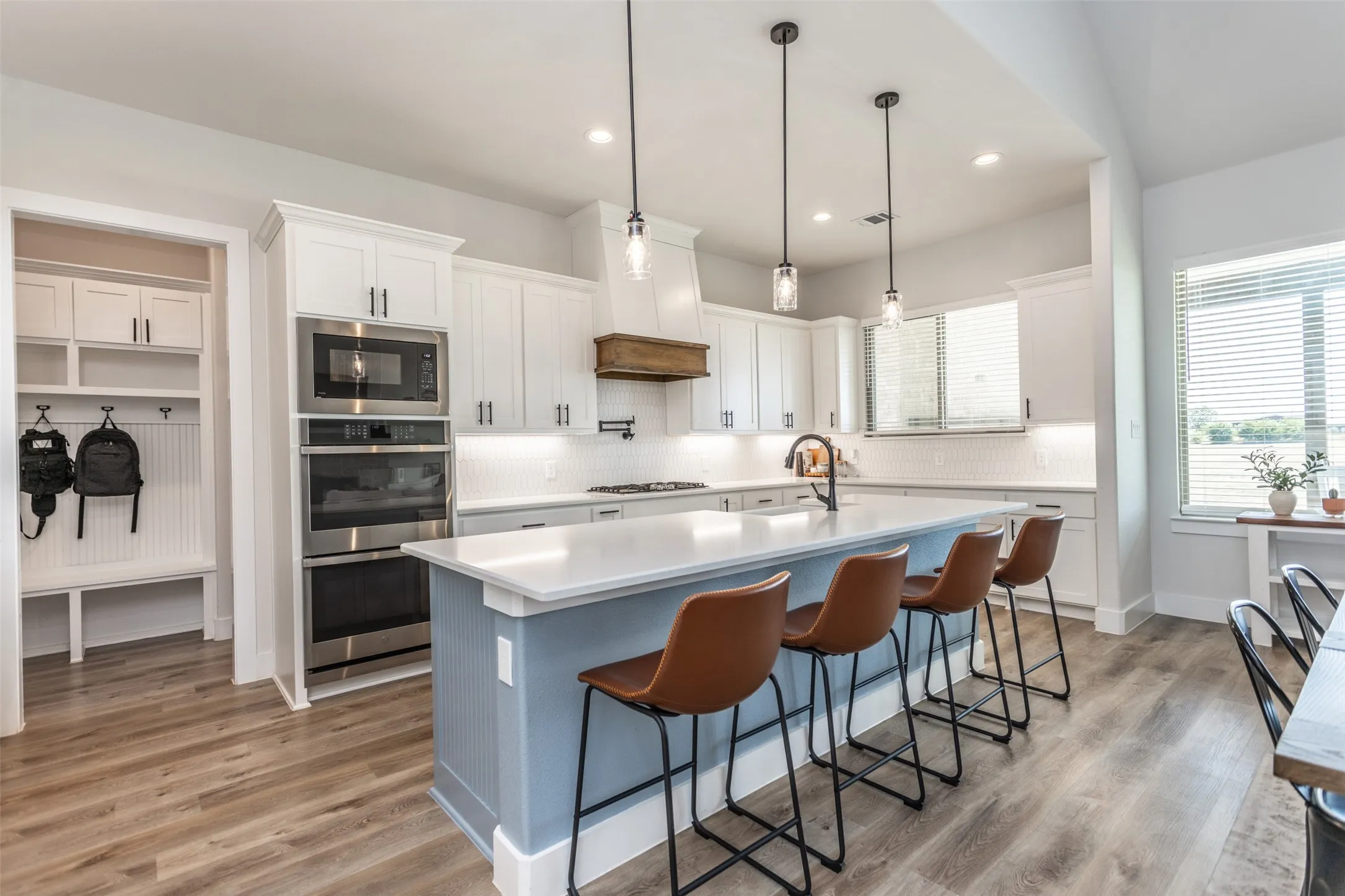 Kitchen featuring a light blue island with counter seating, built-in stainless steel appliances, white cabinetry, and wood-finish flooring