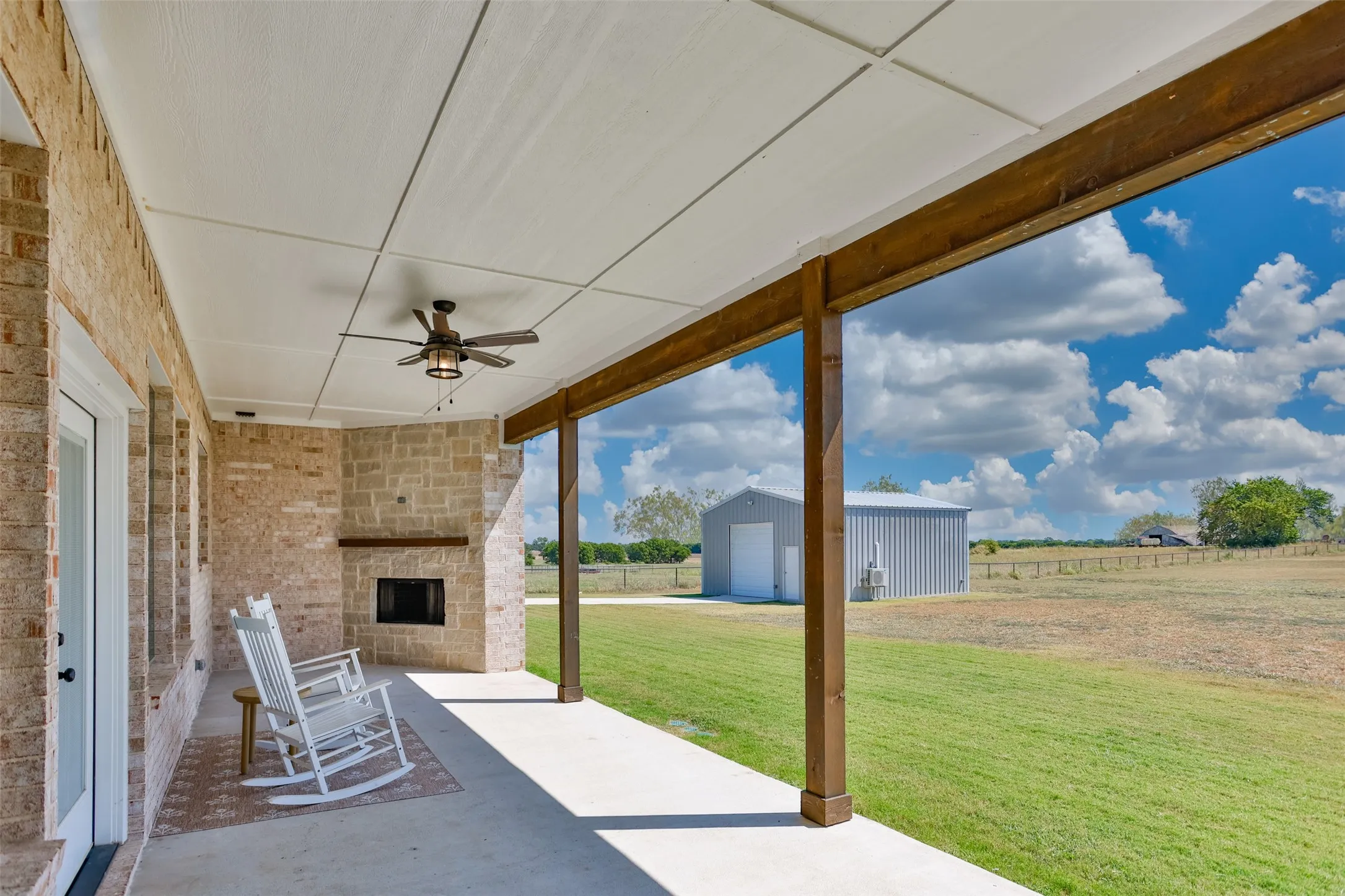 Covered outdoor living area with a stone fireplace, integrated ceiling fan, and exposed wood beams