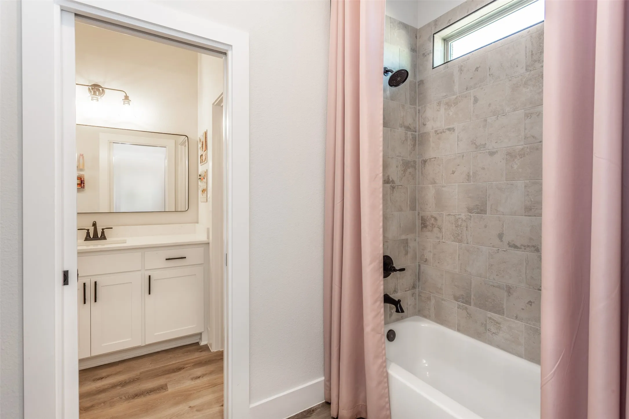 White tub with tiled surround, transom window, and dark fixtures