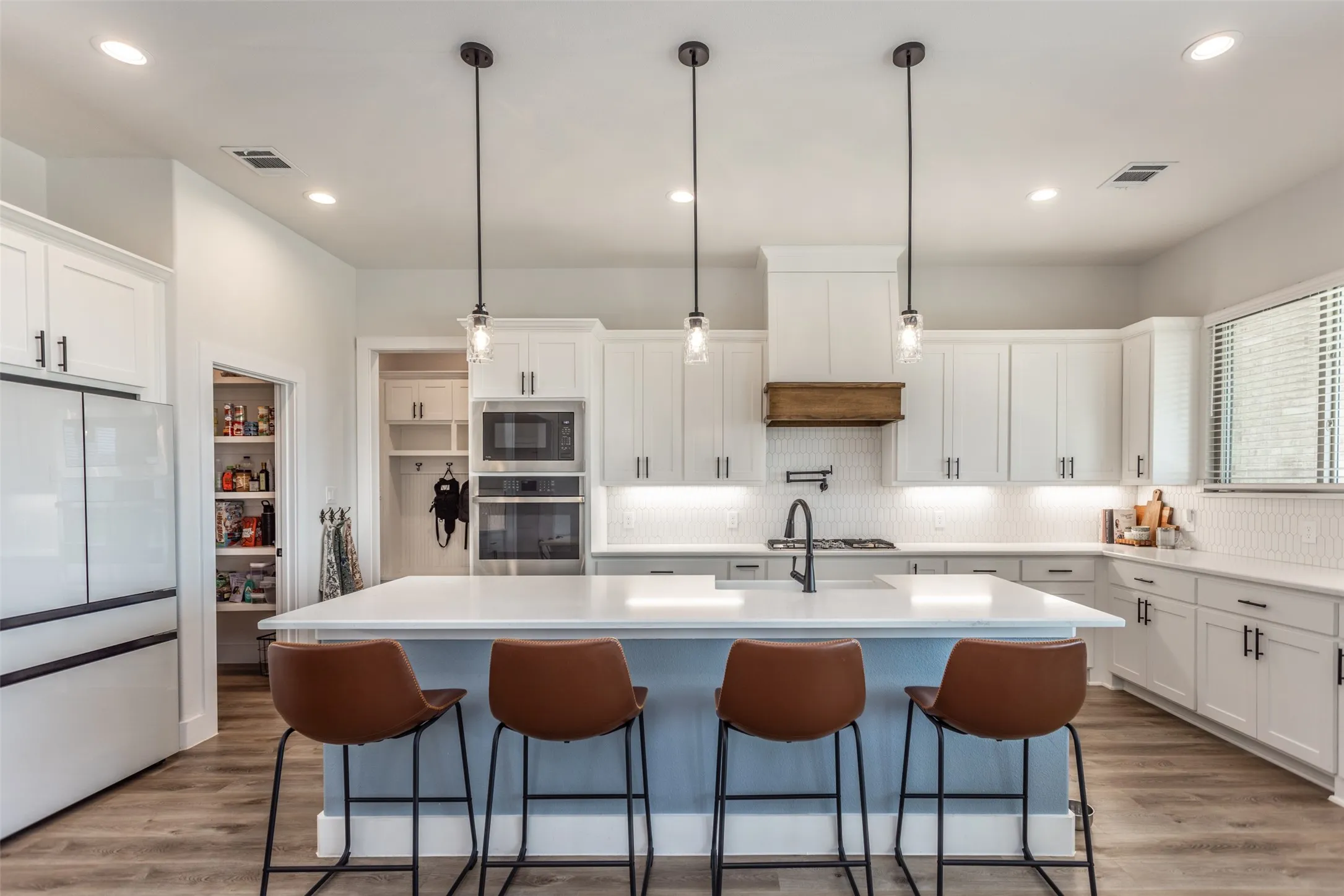 Well-appointed kitchen featuring white cabinetry, a large center island with pendant lighting, integrated stainless steel appliances, and wood-finish flooring