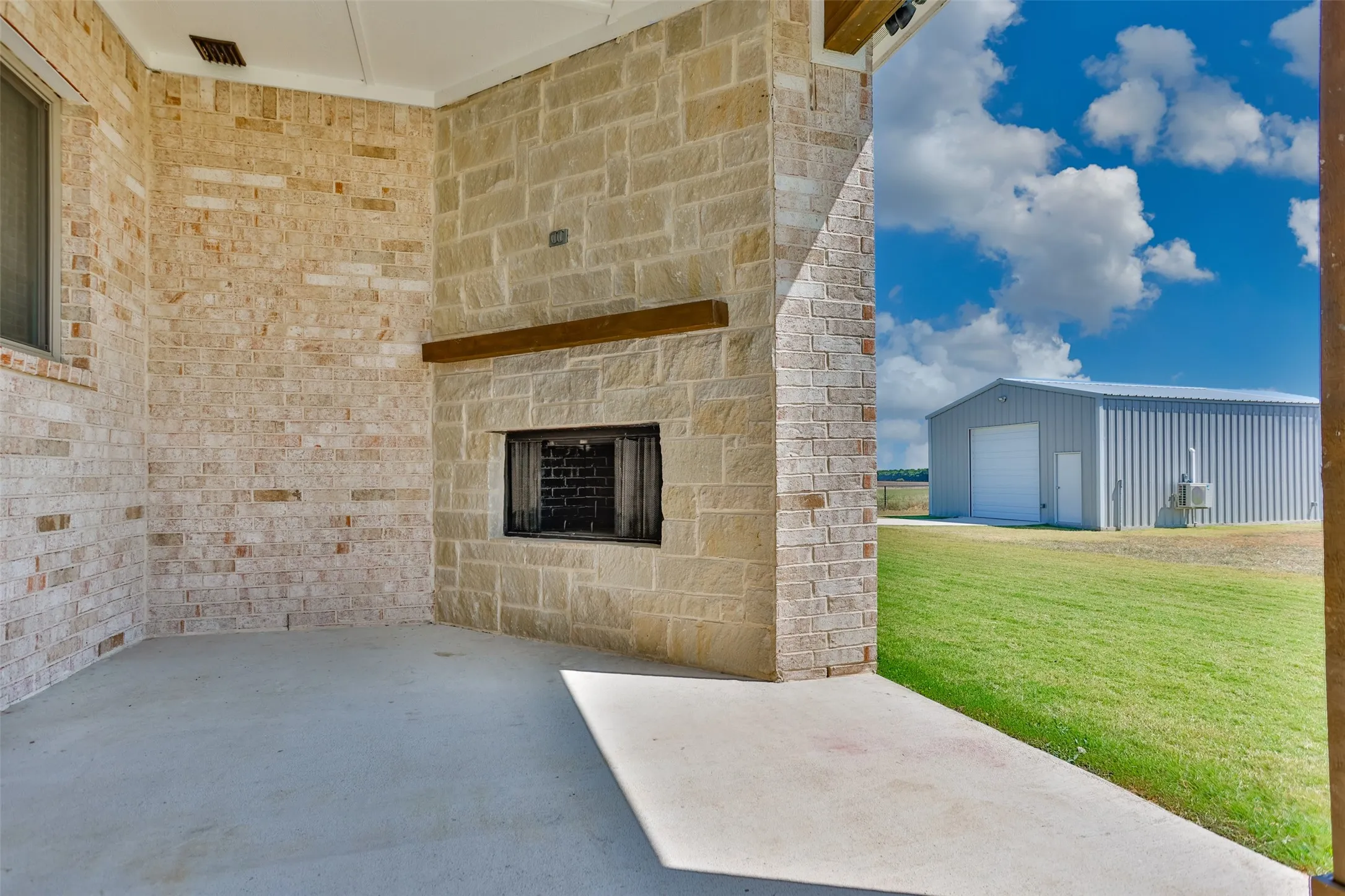 Covered patio featuring a stone fireplace, exposed wood mantel, and concrete flooring