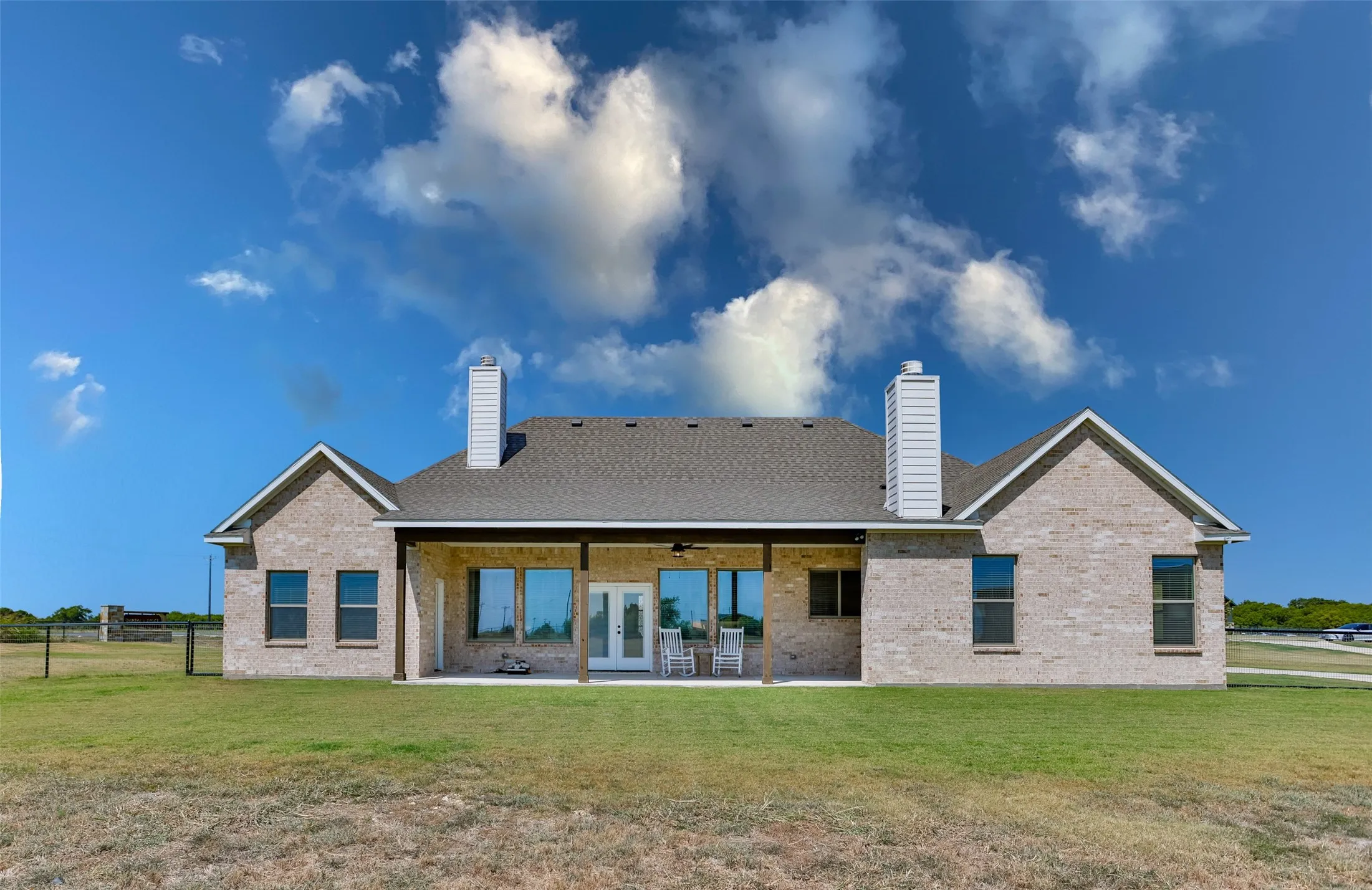 Expansive rear exterior featuring a covered patio, multiple windows, and two prominent chimneys