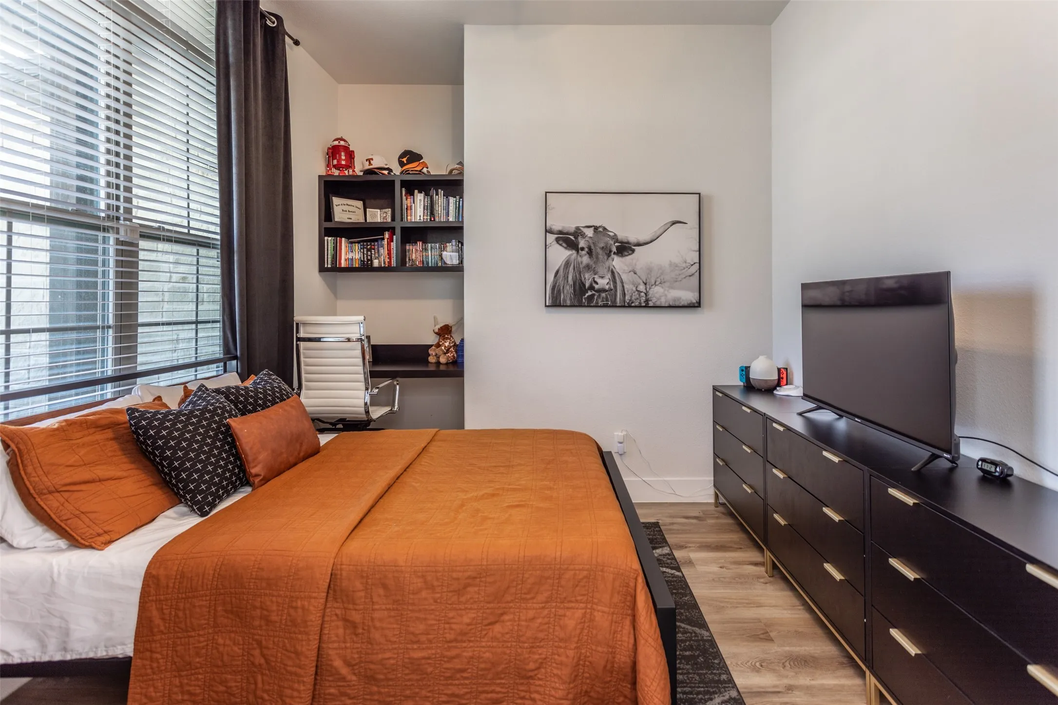 Built-in desk with shelving, window with blinds, and wood-finish flooring