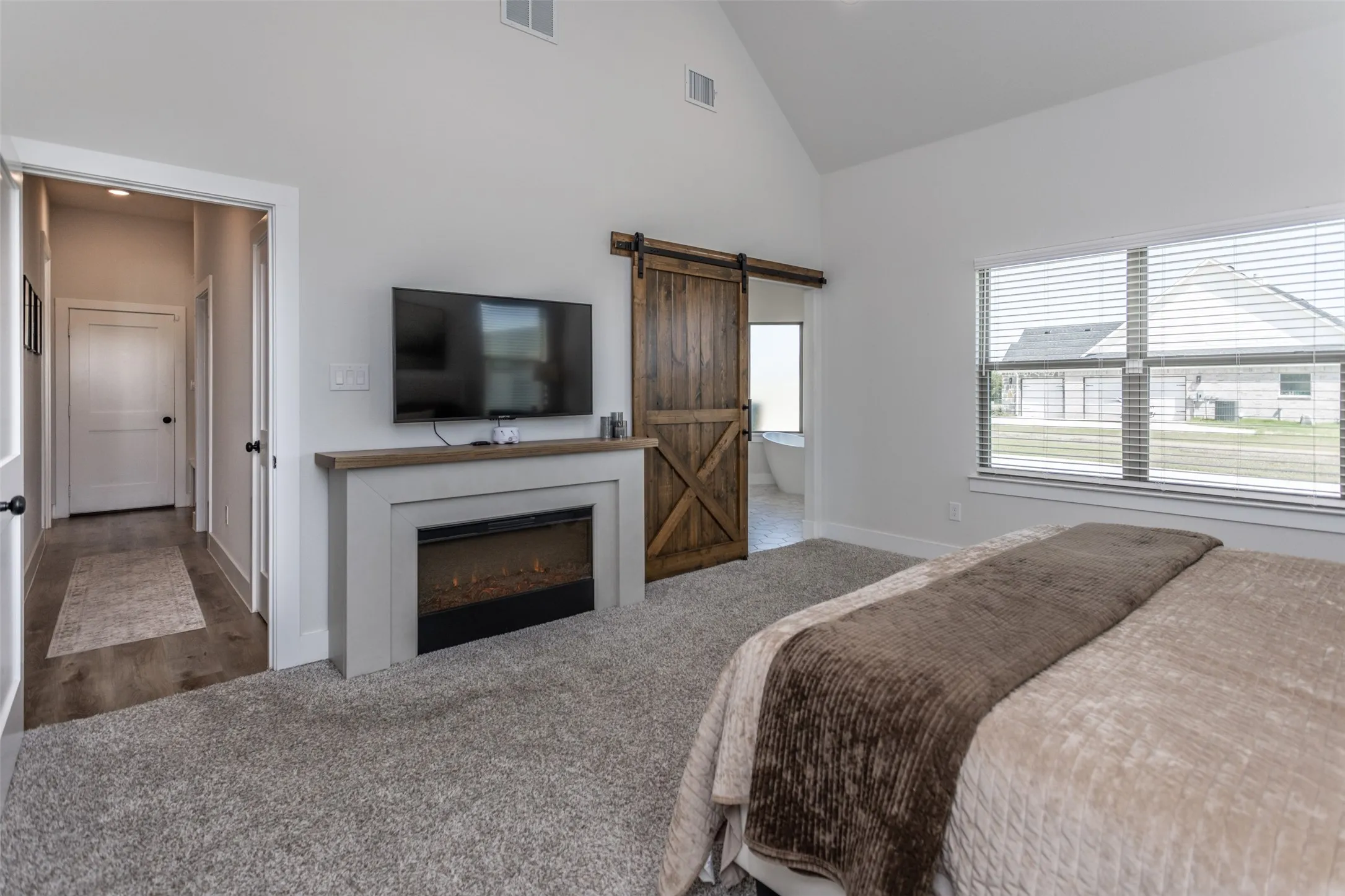 Vaulted ceiling, built-in electric fireplace, wood-finish mantel, barn door, and large window with blinds