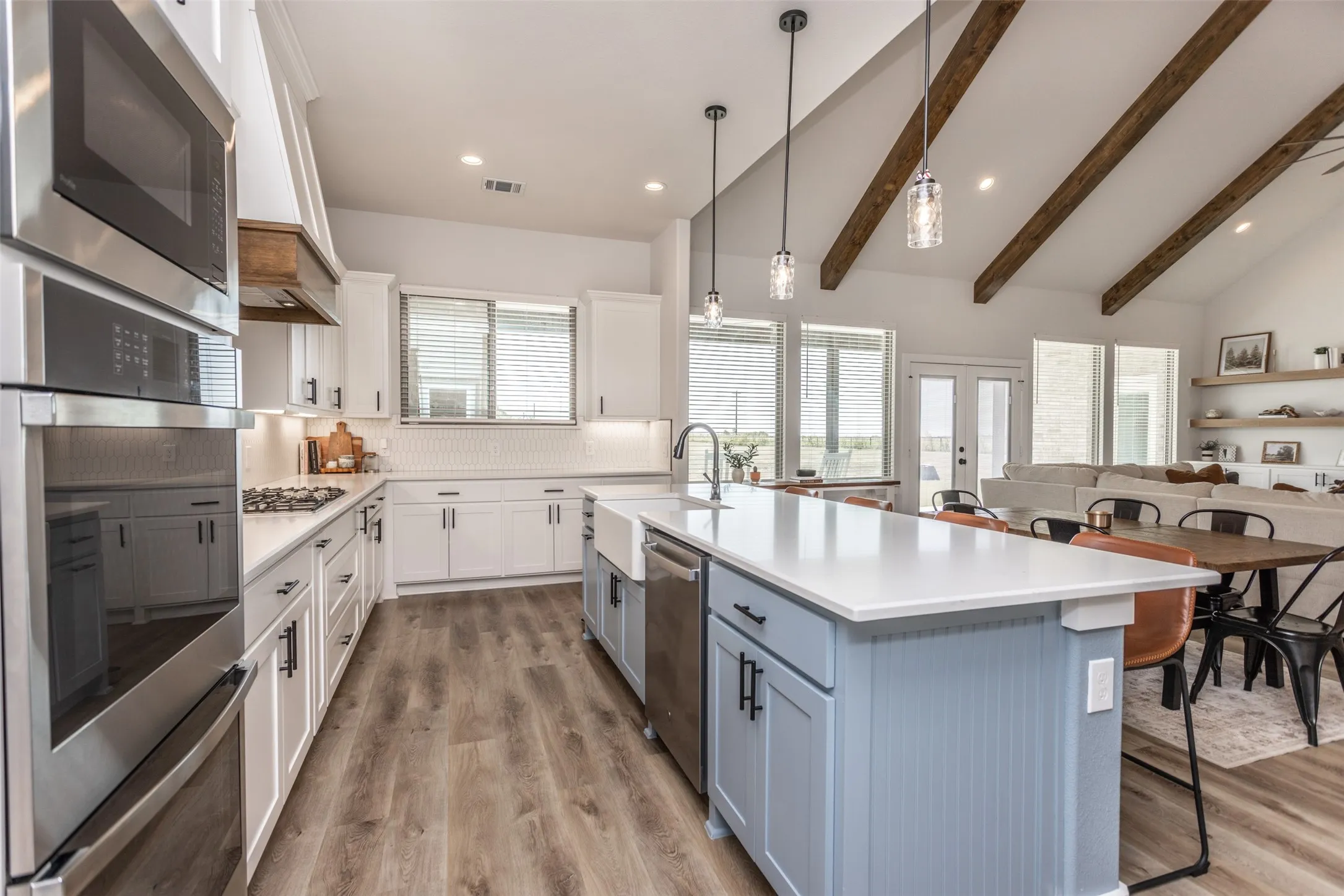 Gourmet kitchen featuring stainless steel appliances, wood-finish flooring, a double basin farmhouse sink, an expansive island with a light blue cabinet finish, and a gas range