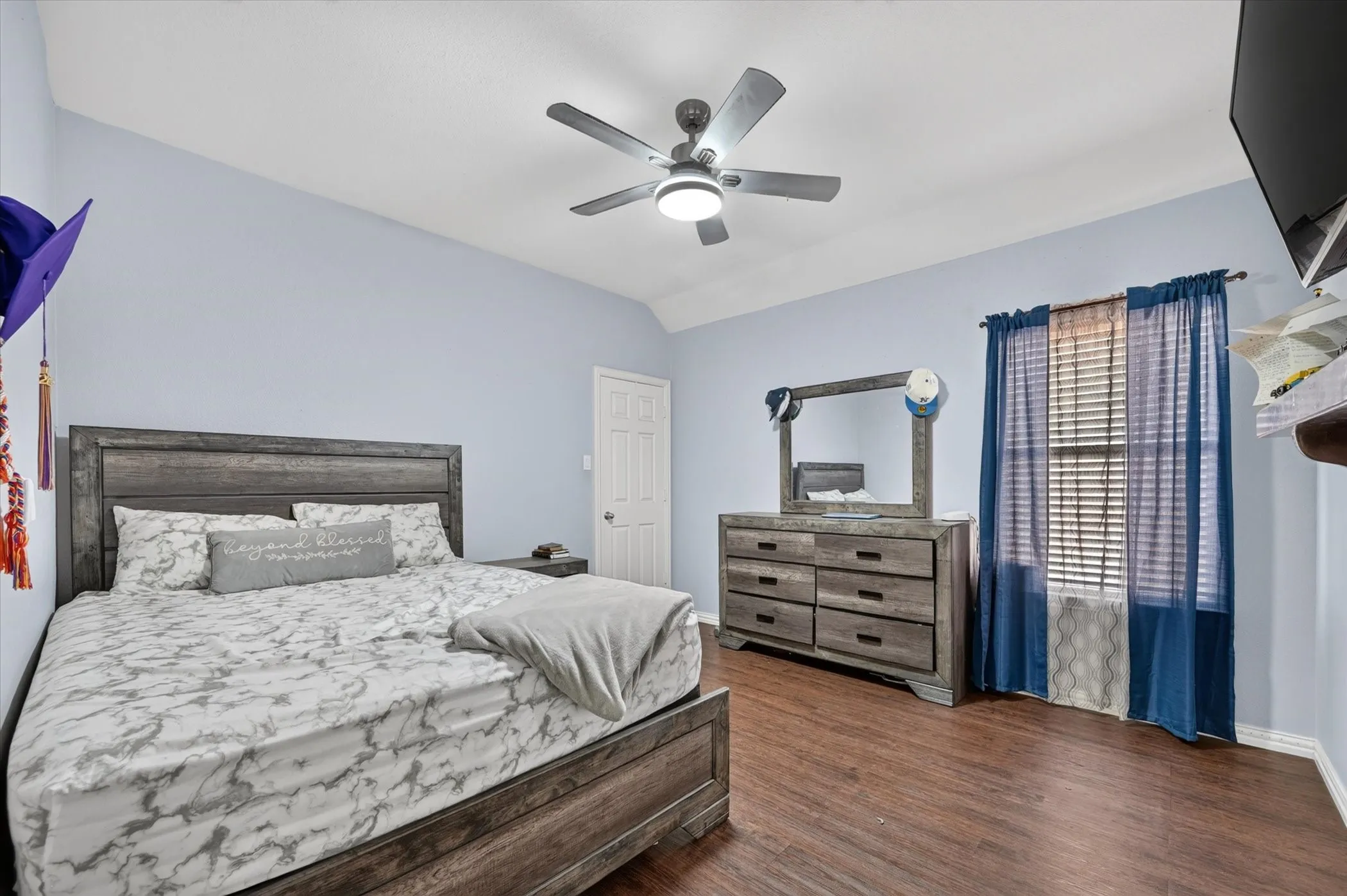 Vaulted ceiling, ceiling fan with integrated lighting, wood-finish flooring, window with blinds, and white trim