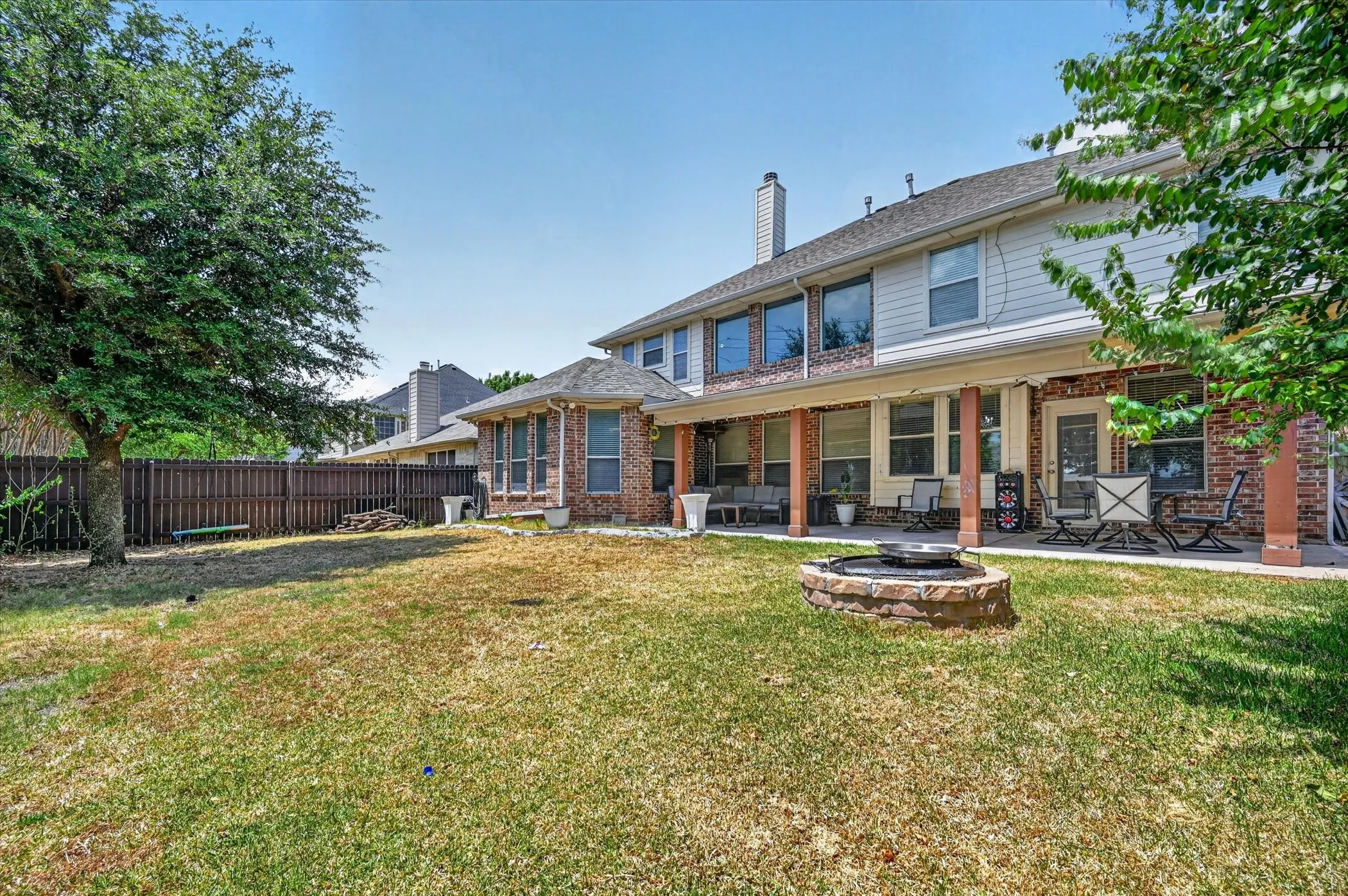 Expansive backyard featuring a stone fire pit, covered patio, brick and siding exterior, and a privacy fence