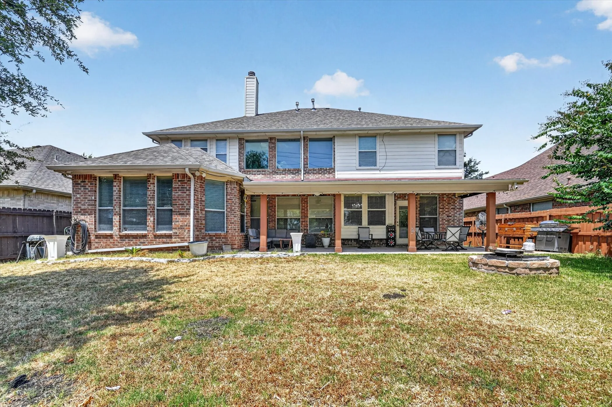 Expansive backyard featuring a covered patio, stone fire pit, and brick exterior