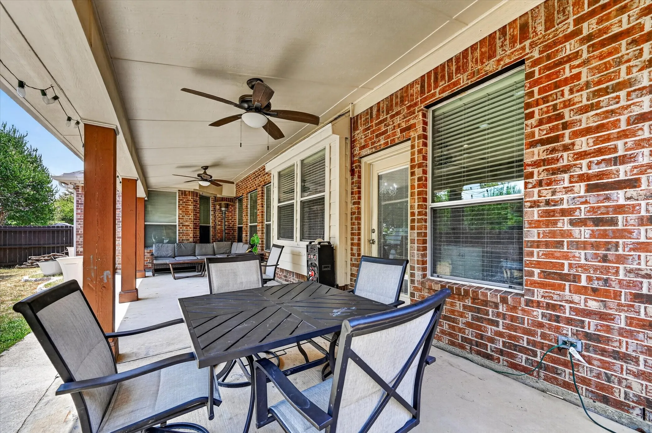 Covered patio with brick exterior, concrete flooring, and multiple ceiling fans