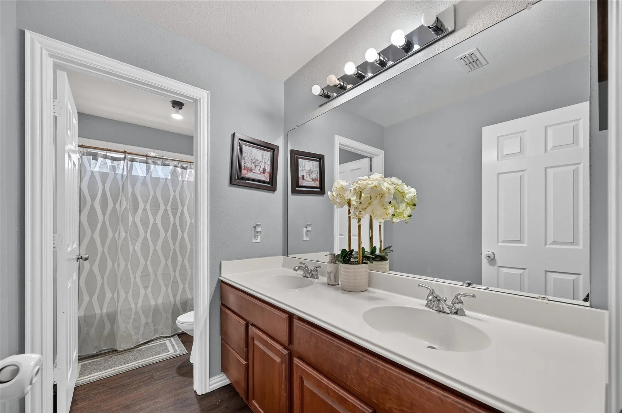 Dual vanity with wood-finish cabinetry, white countertops, and chrome fixtures
