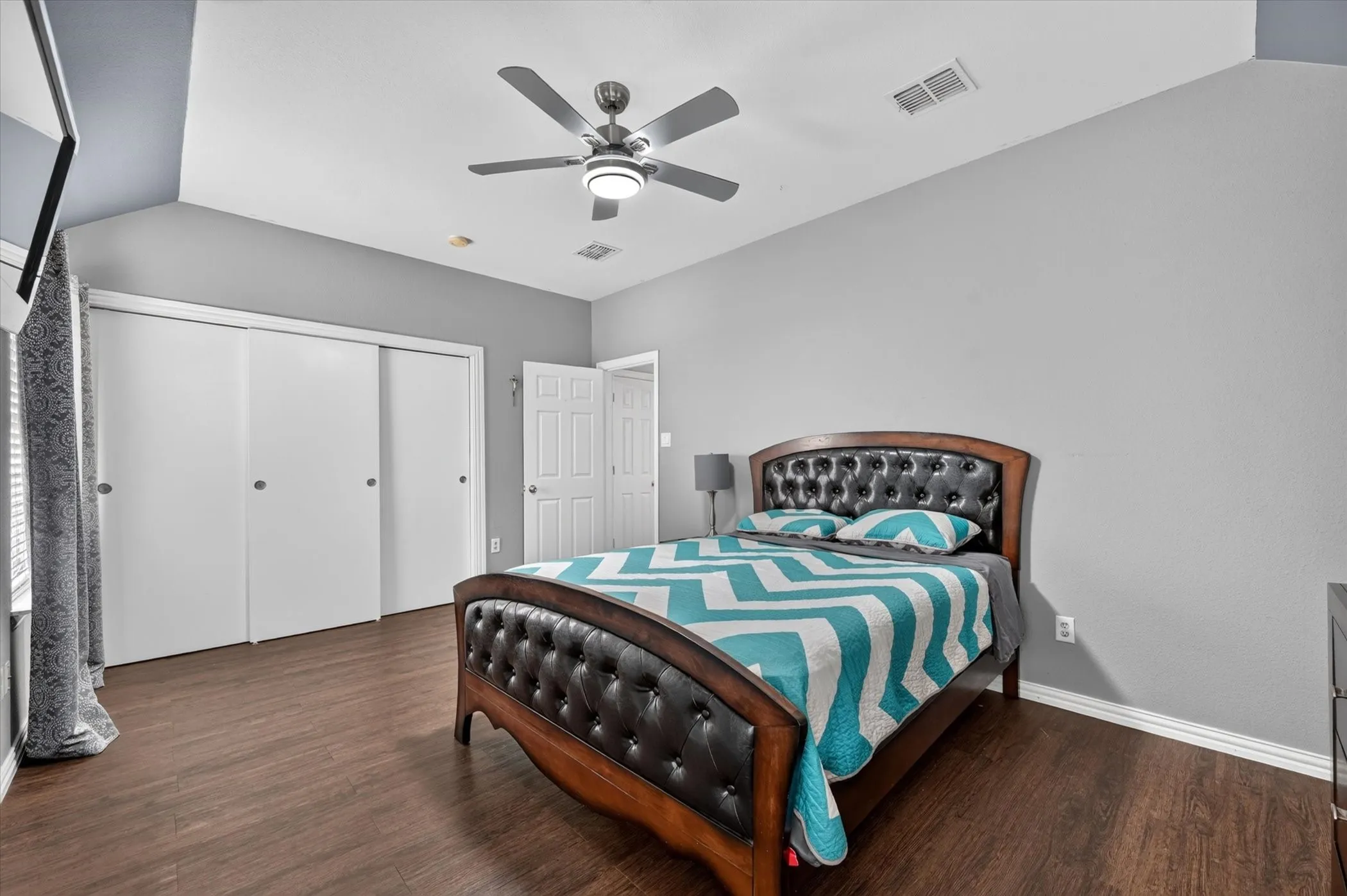 Vaulted ceiling featuring a ceiling fan with integrated lighting, wood-finish flooring, and sliding closet doors