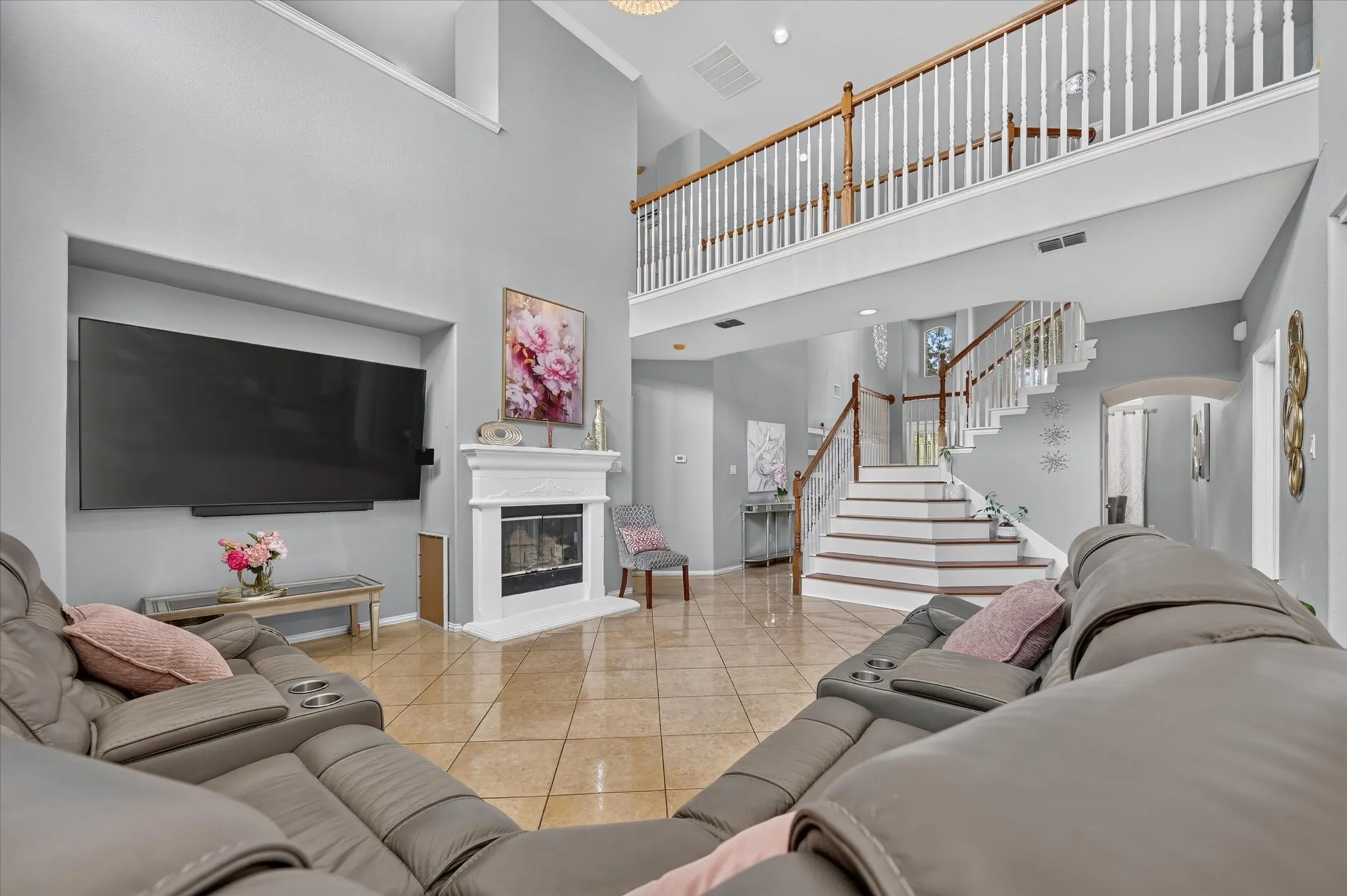 Two-story living area featuring a fireplace with a white mantel, tile flooring, and a second-story landing with wood and white railings