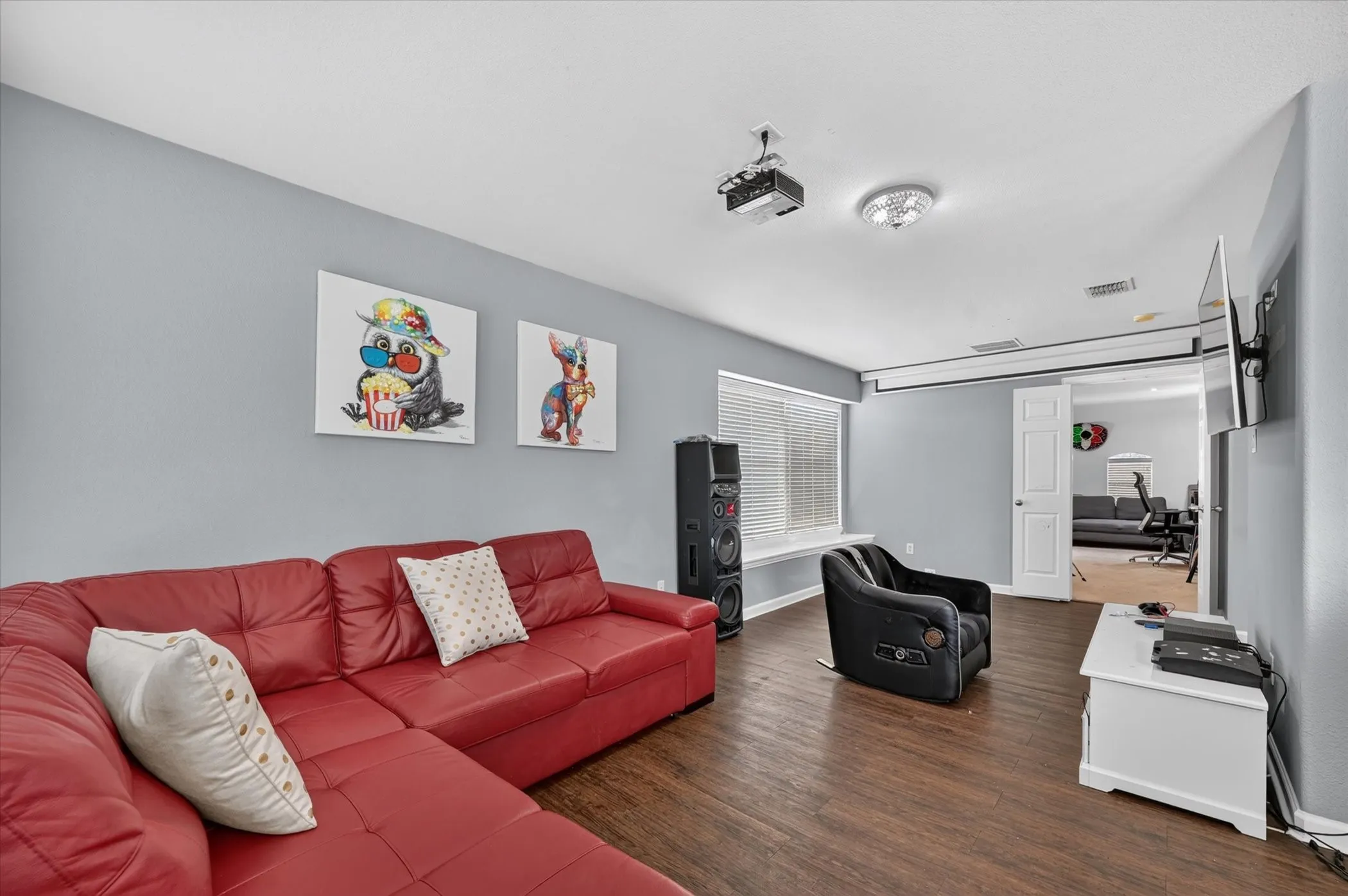 Wood-finish flooring, recessed lighting, ceiling-mounted projector, wall-mounted television, and a window with blinds