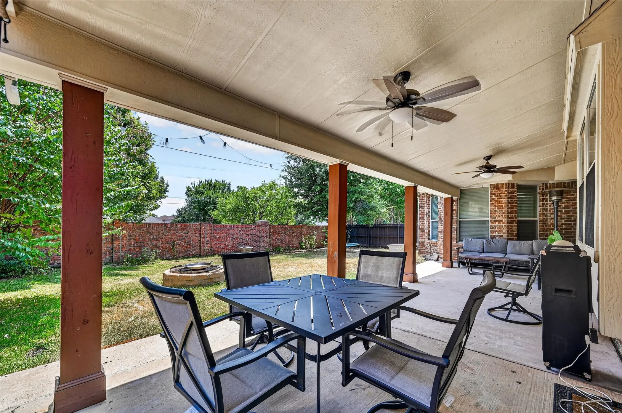 Expansive covered patio with multiple ceiling fans, concrete flooring, and brick-column accents