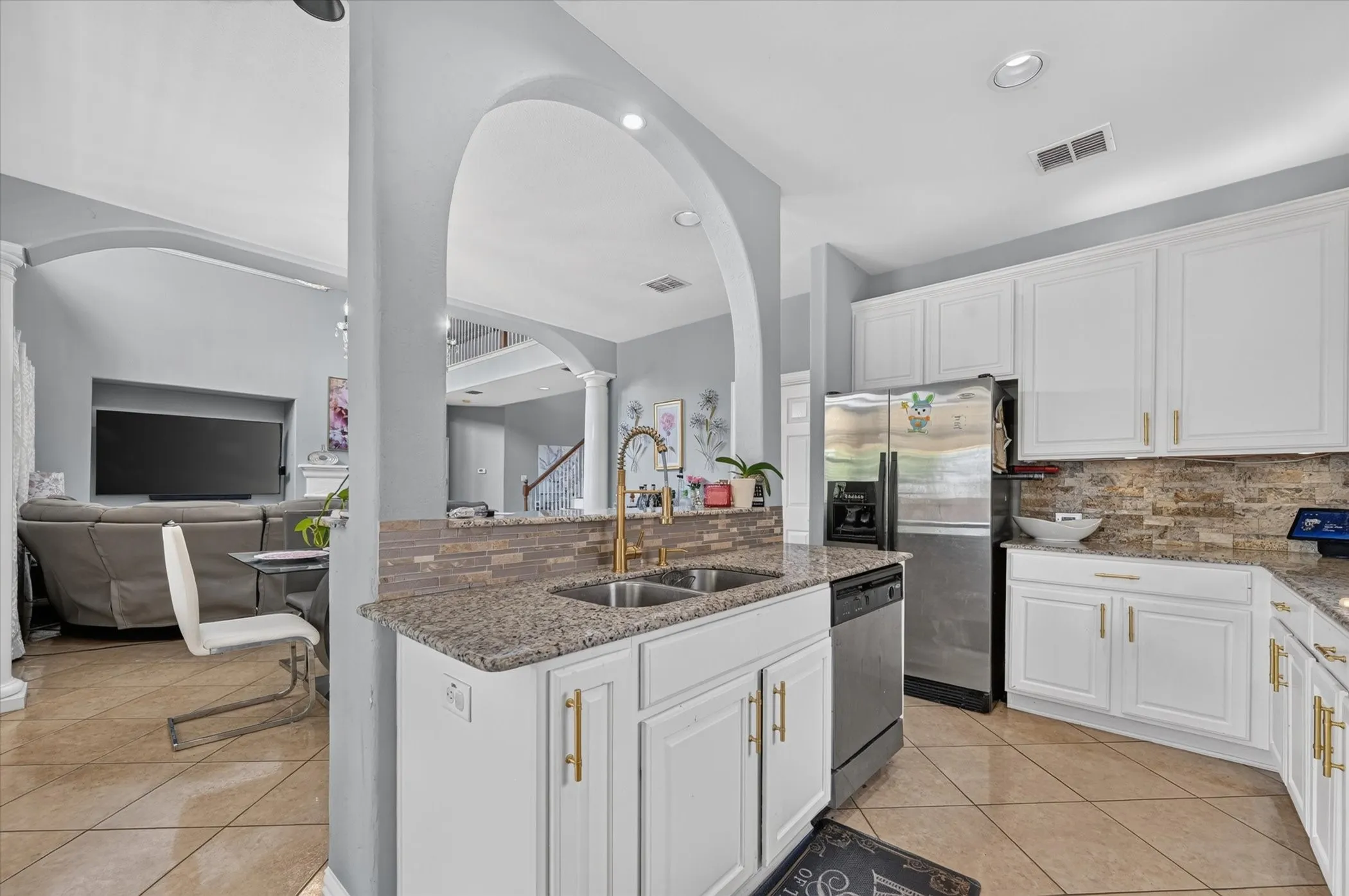 Kitchen featuring granite countertops, white cabinetry with gold-tone hardware, stainless steel appliances, and a tiled backsplash