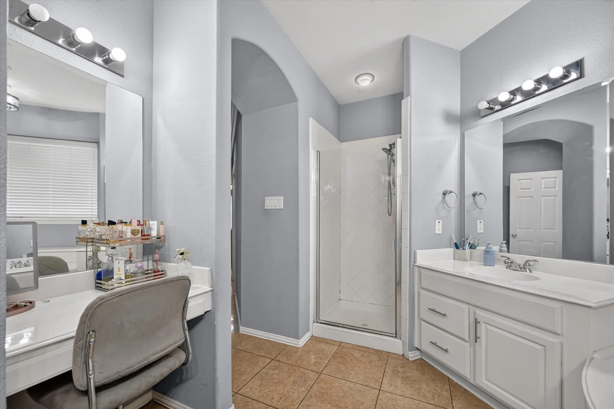 Dual vanity areas with integrated mirrors, a glass-enclosed shower, and tile flooring