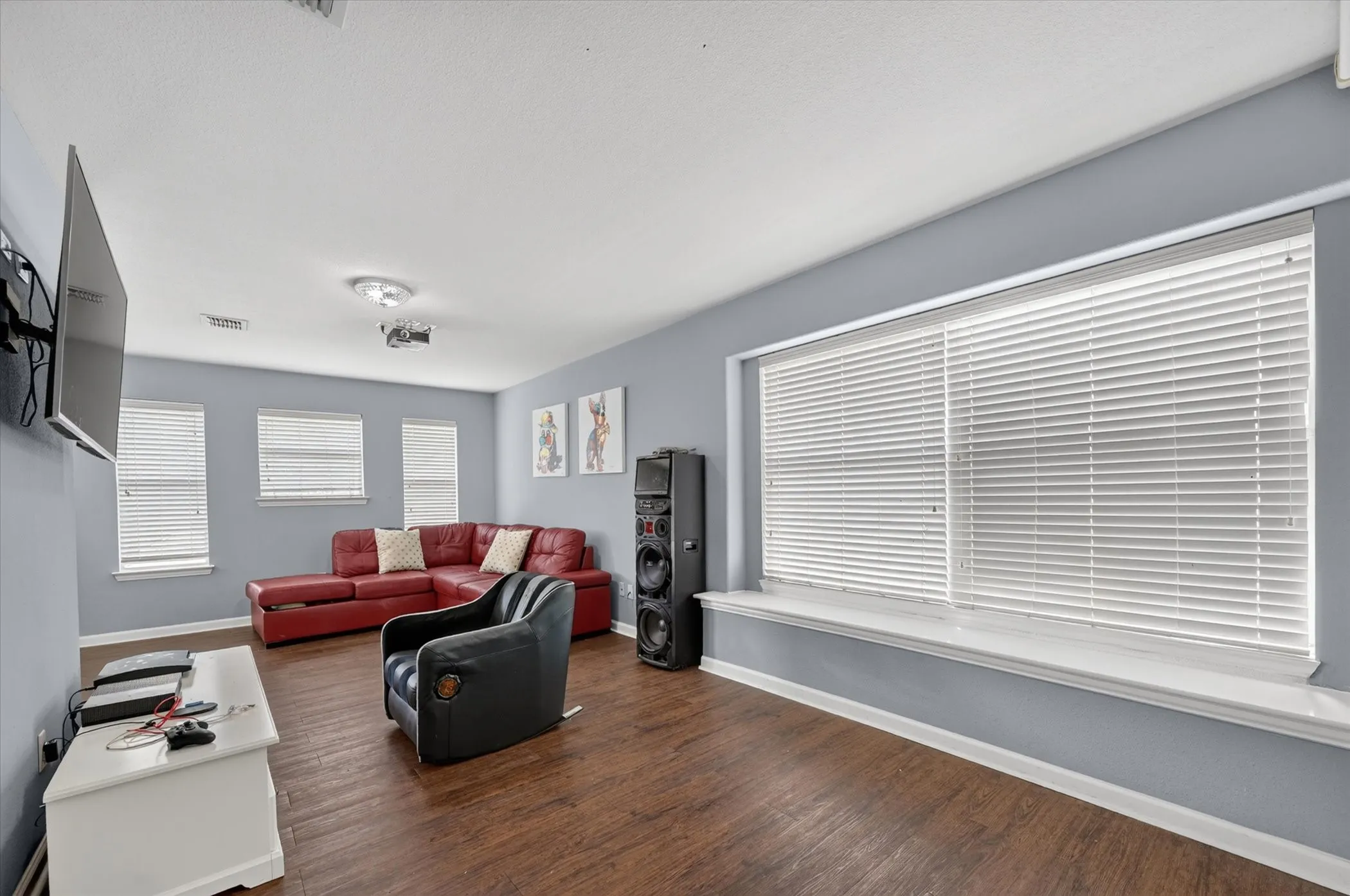 Spacious room featuring wood-finish flooring and multiple windows with blinds
