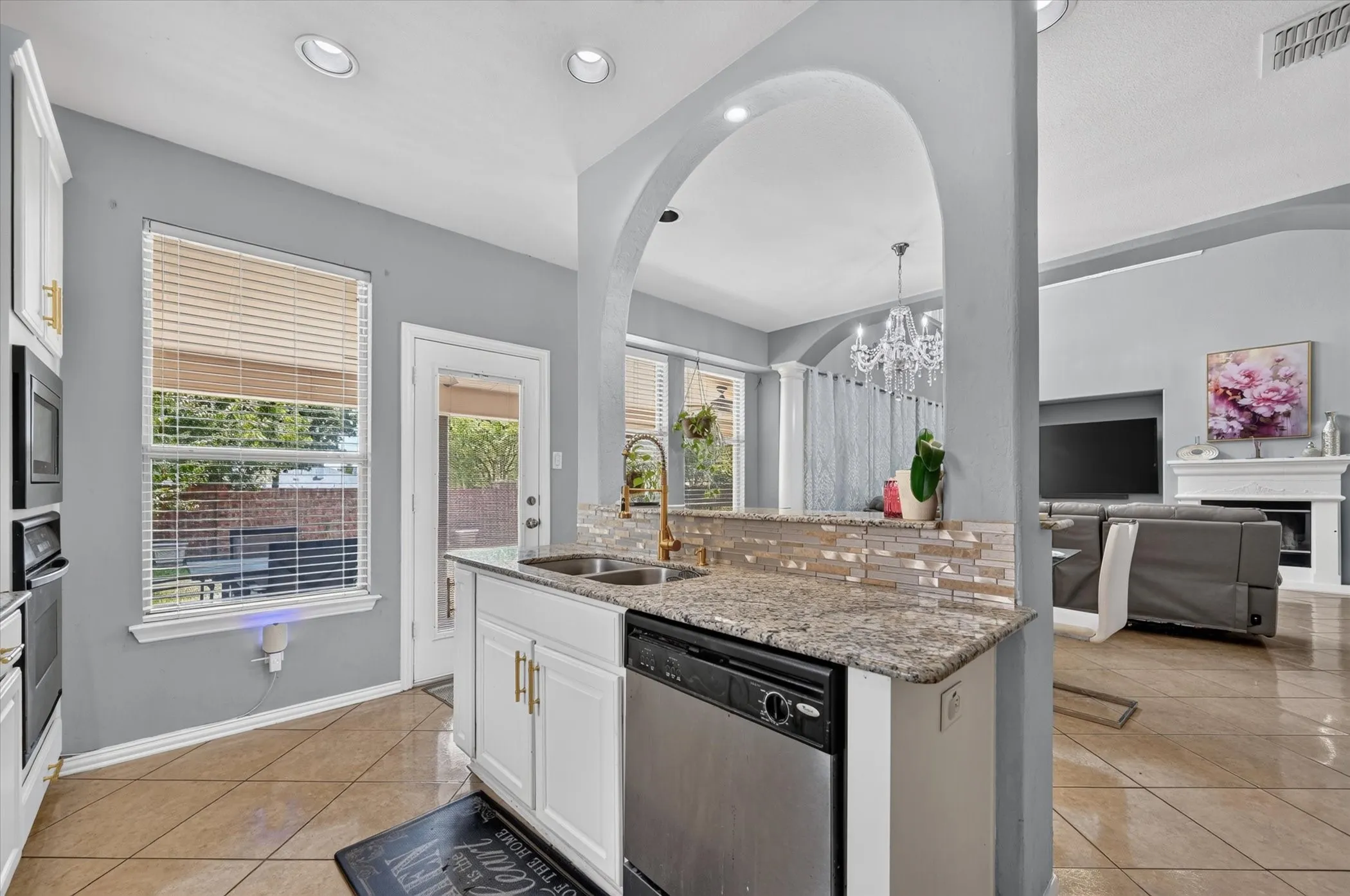 Kitchen with tile flooring, white cabinetry, granite-finish countertops, stainless steel sink, and a tiled backsplash