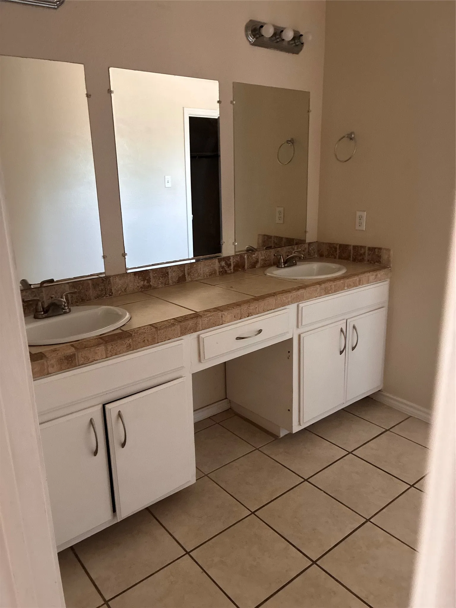 Double vanity with integrated sinks, tiled countertop and backsplash, white cabinetry, and ceramic tile flooring