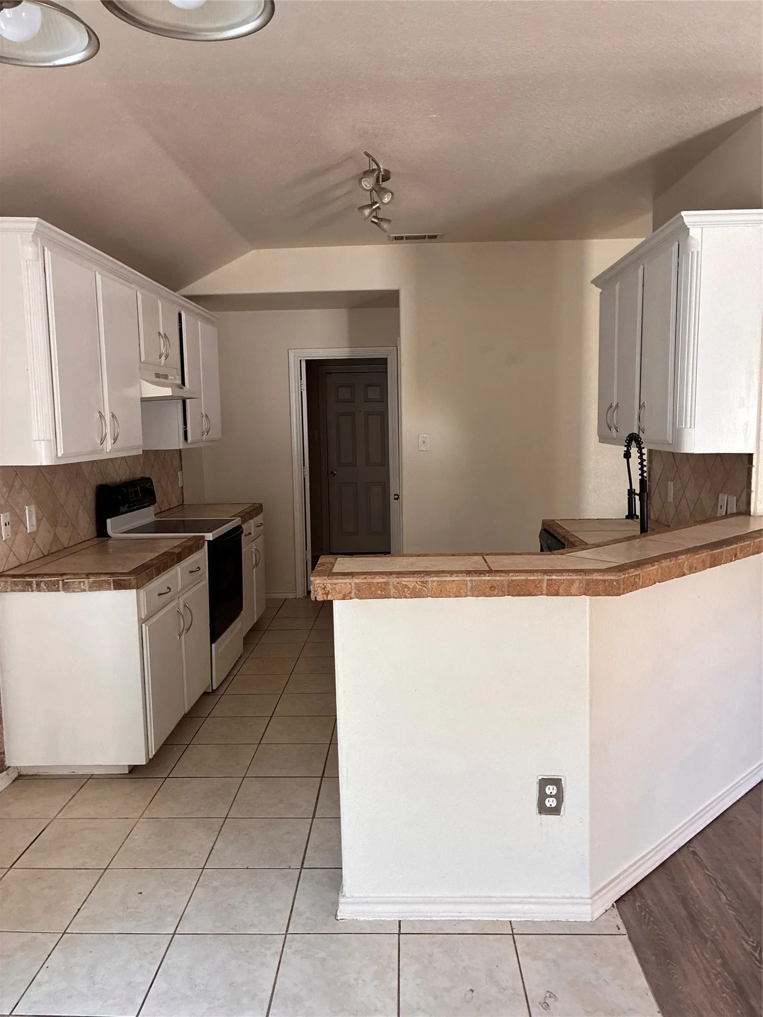 Kitchen featuring white cabinetry, tile countertops, an integrated sink with a black pull-down faucet, and a black range