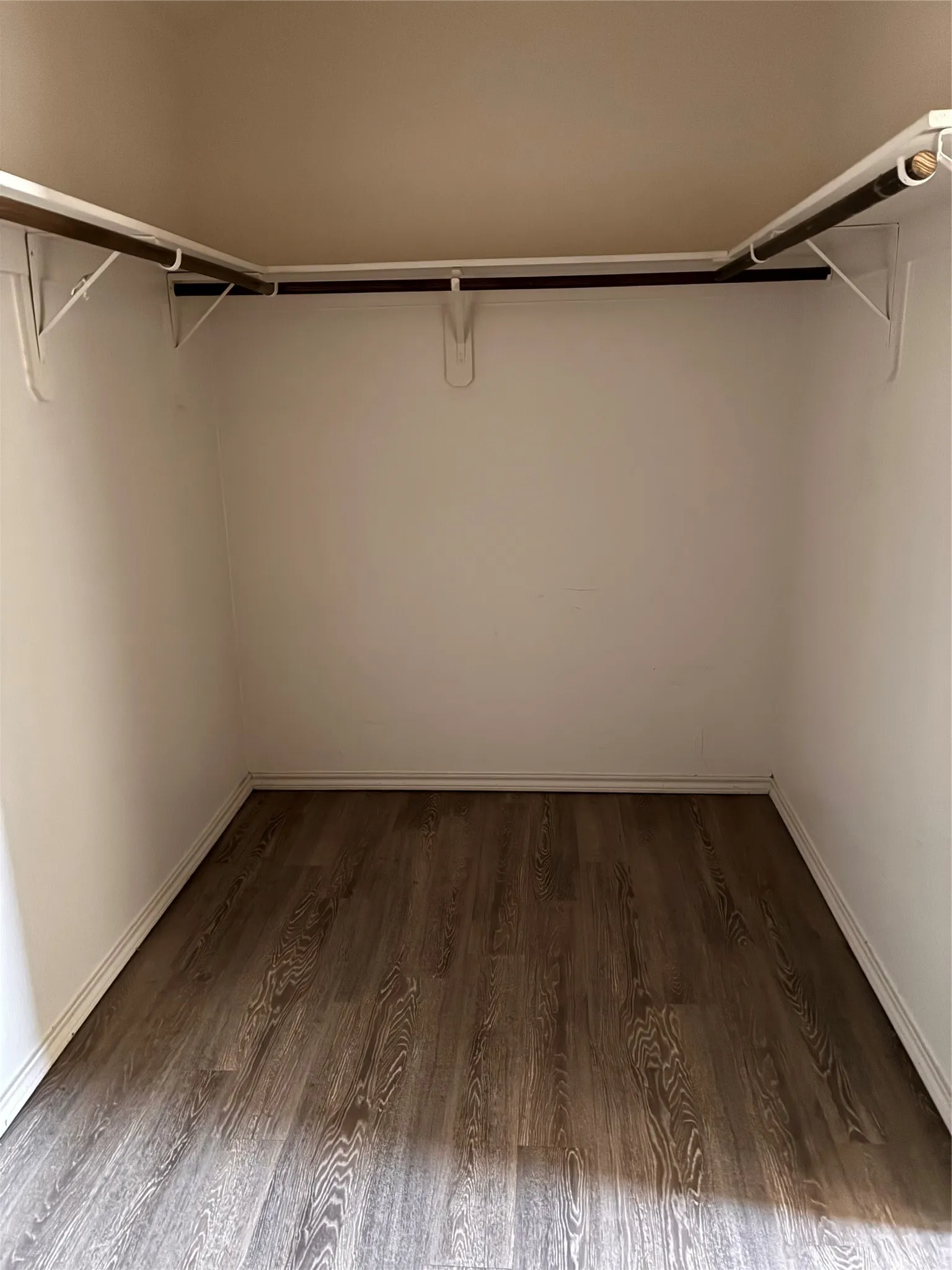 Closet featuring wood-finish flooring, white walls, and built-in clothes rods