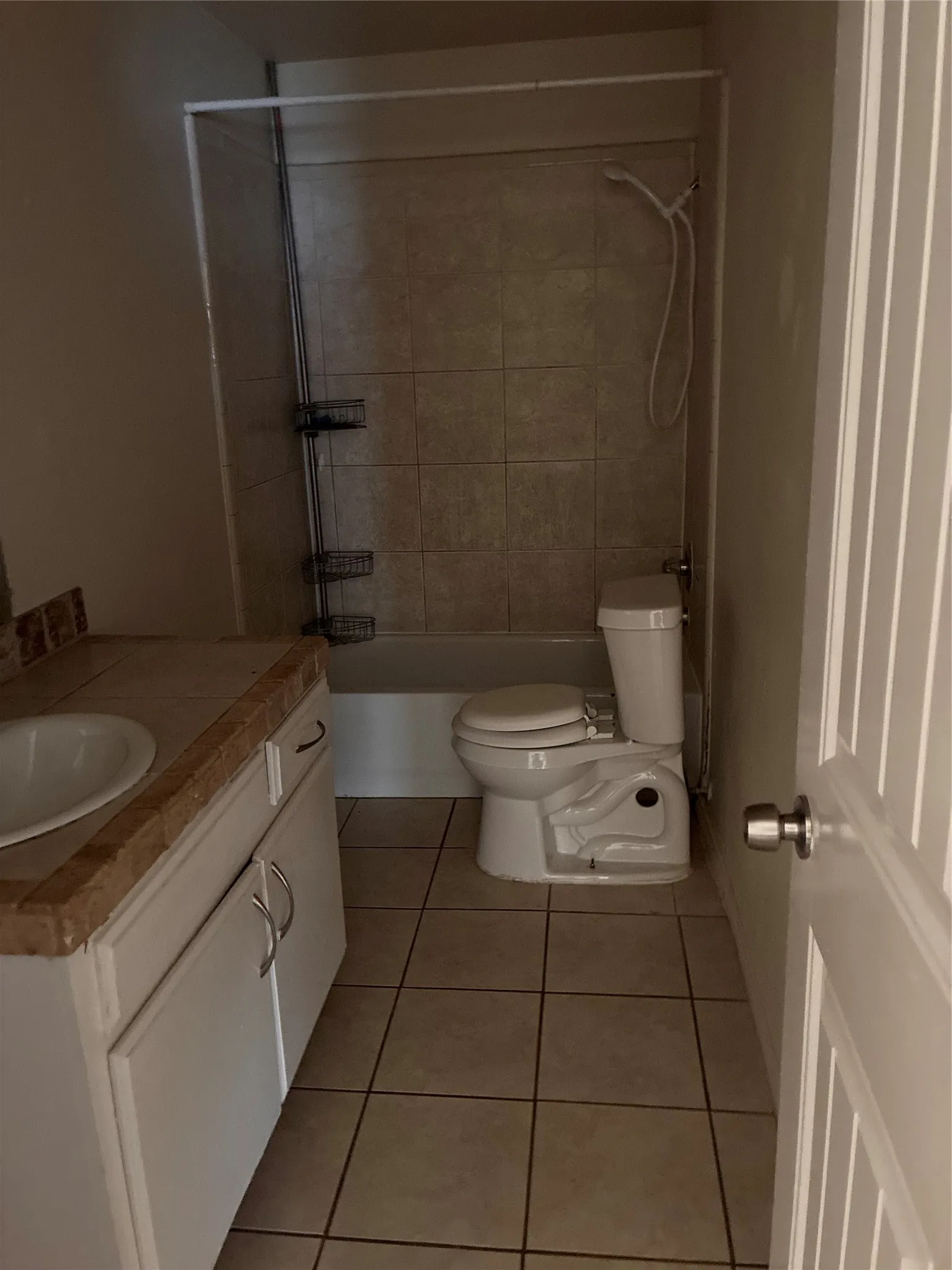 Tile flooring, white vanity with integrated sink, tiled shower surround, and white toilet
