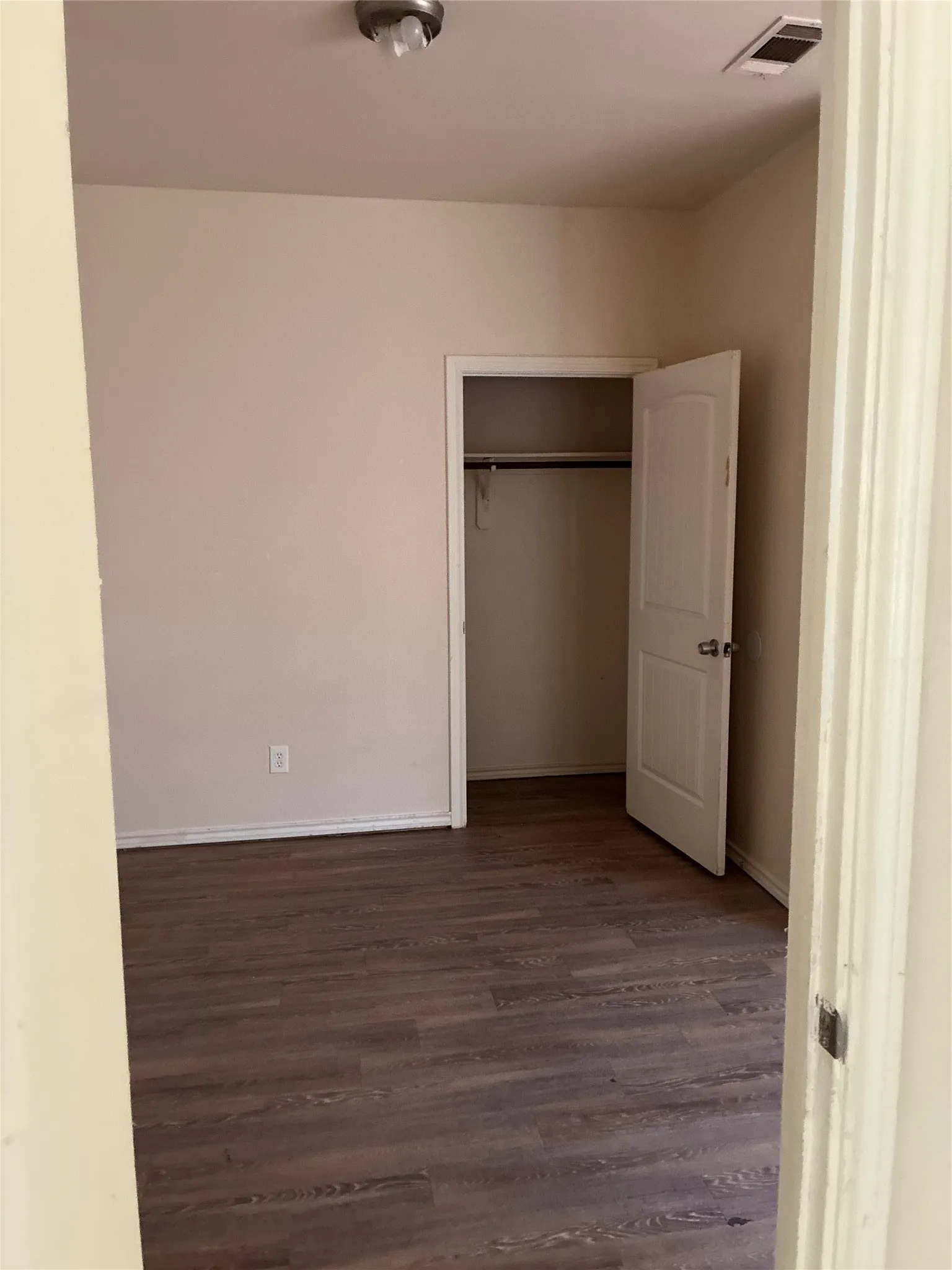 Wood-finish flooring with a neutral wall color, featuring a built-in closet with a panel door, and a ceiling-mounted light fixture