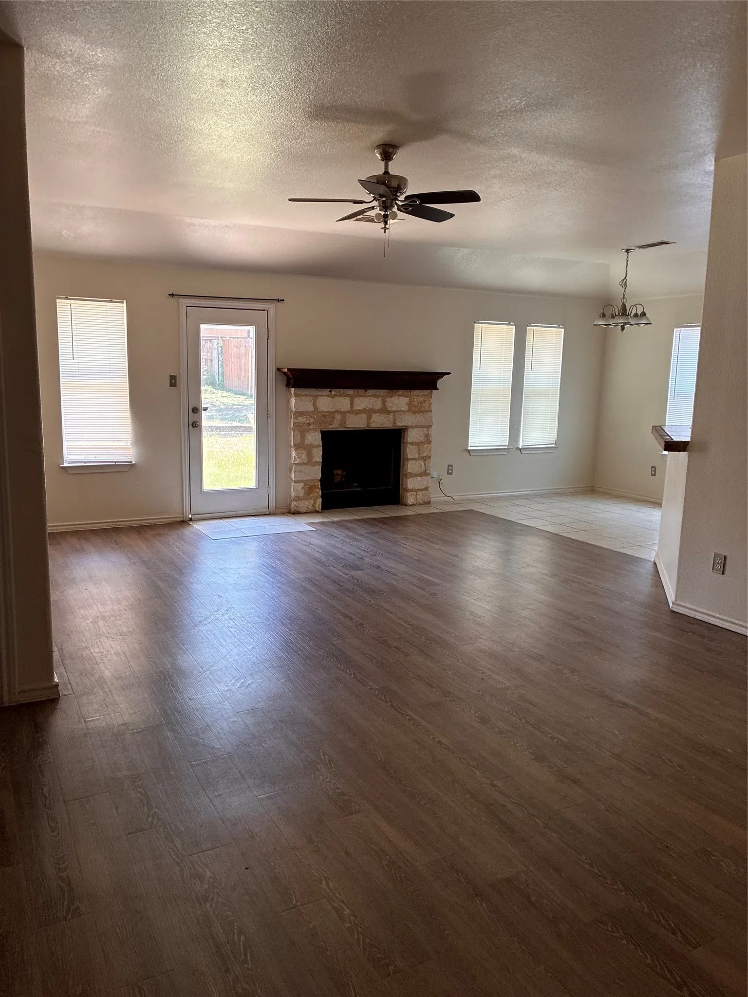 Spacious living area featuring wood-finish flooring, a stone-surround fireplace with a wood mantle, and a ceiling fan