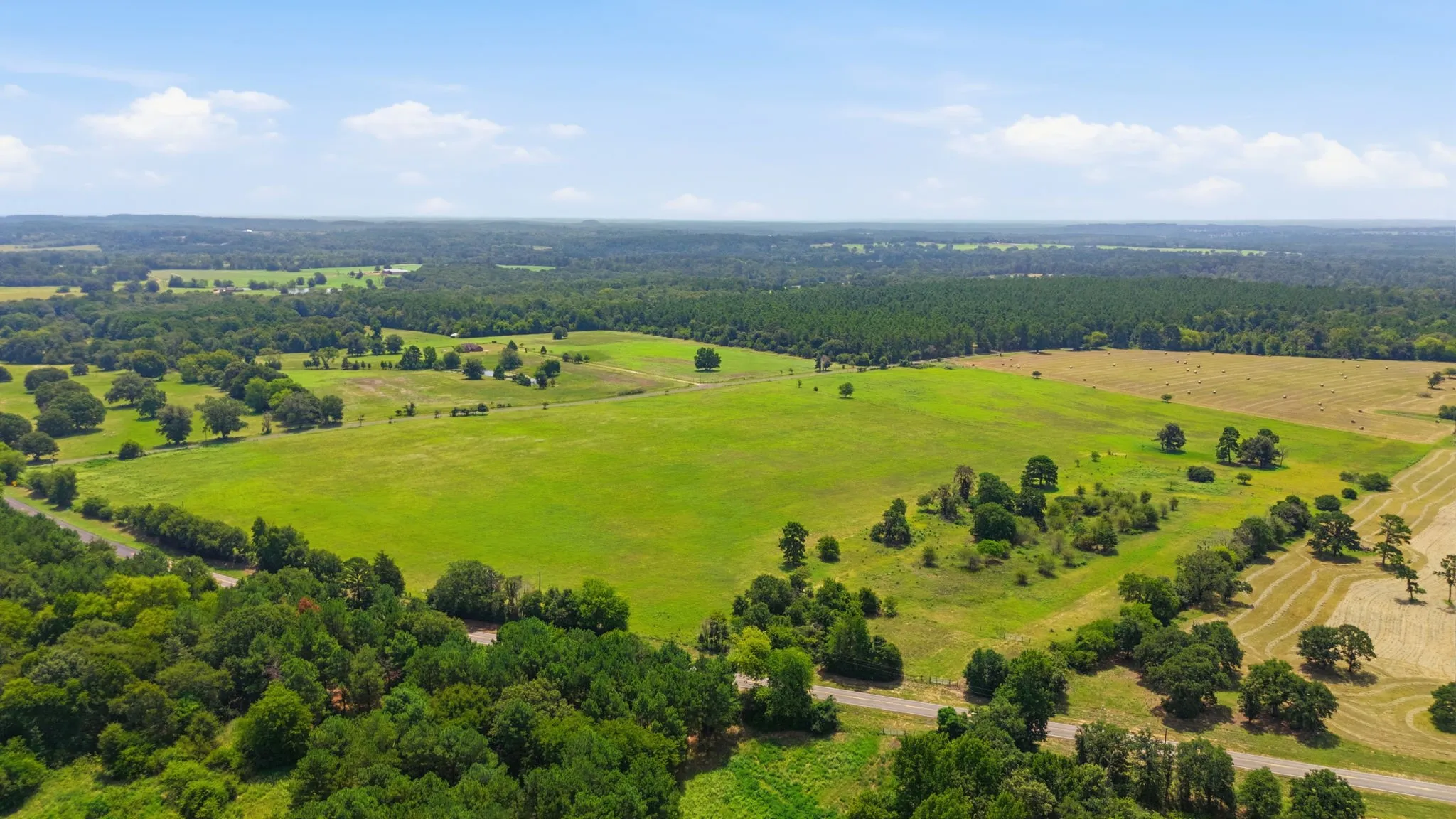 Expansive green fields, mature trees, and varied terrain, all under a clear sky