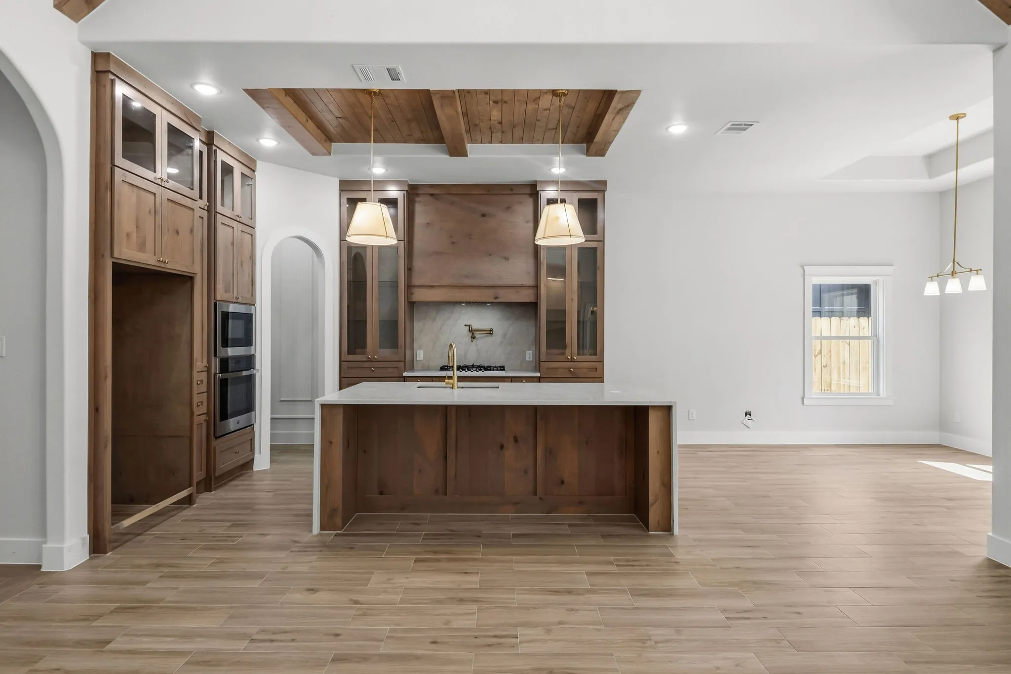 Central island with integrated sink, wood-finish flooring, double wall ovens, wood beam ceiling feature, and arched doorways