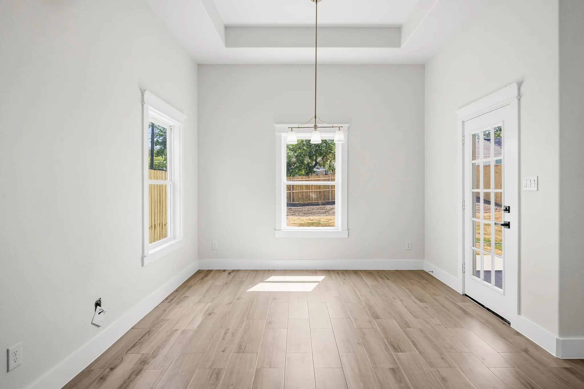 Wood-finish flooring, white walls, two windows with white trim, and a tray ceiling