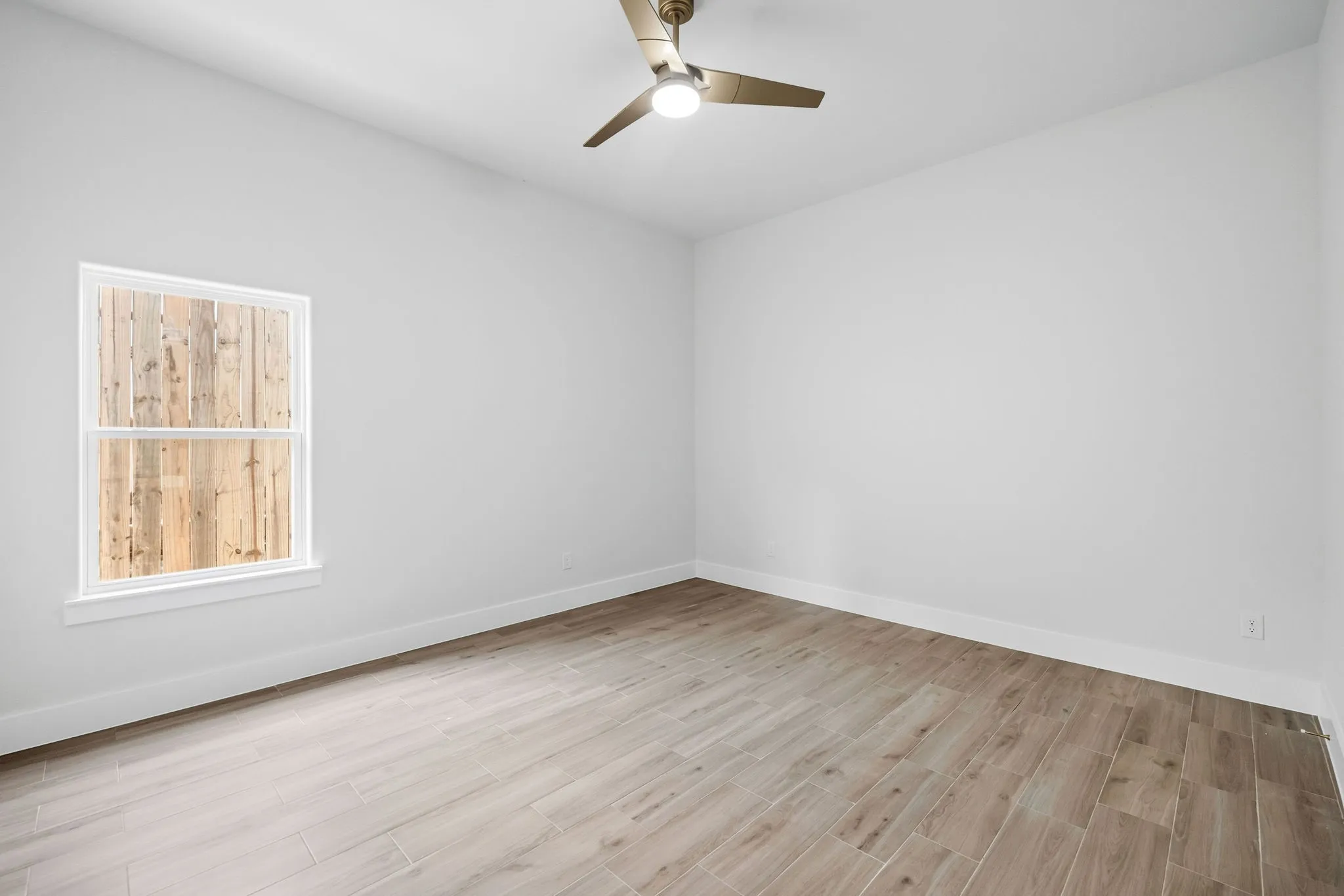 Neutral color palette with wood-finish flooring, a ceiling fan with integrated lighting, and a double-hung window