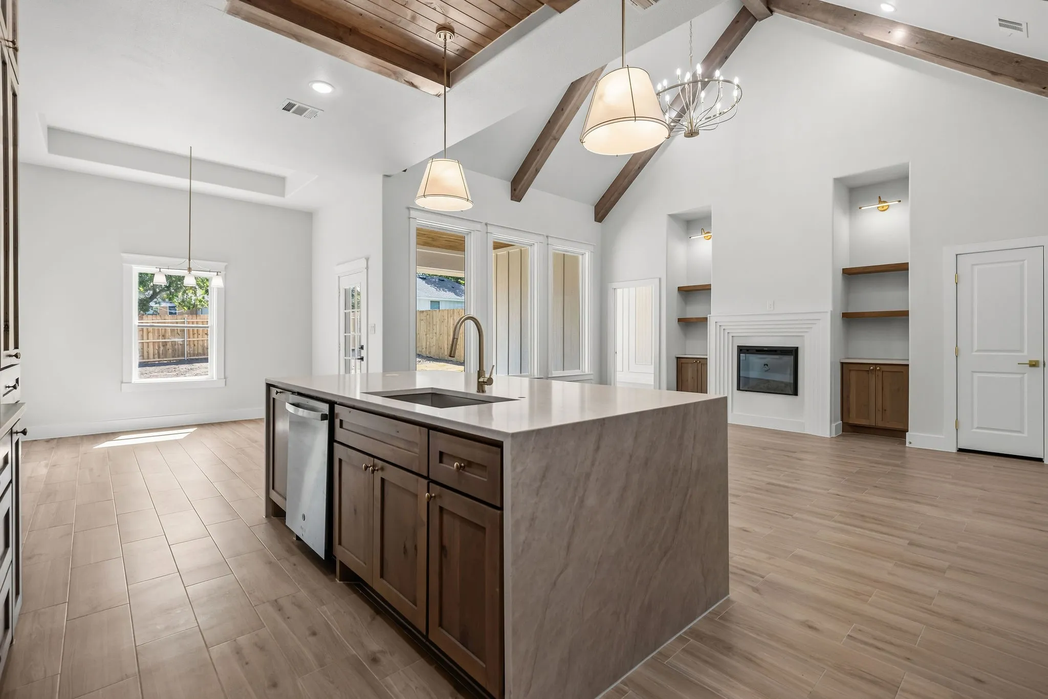 Open-concept living space featuring a vaulted wood-beam ceiling, a built-in fireplace with flanking shelving, a central kitchen island with a built-in sink, and wood-finish flooring