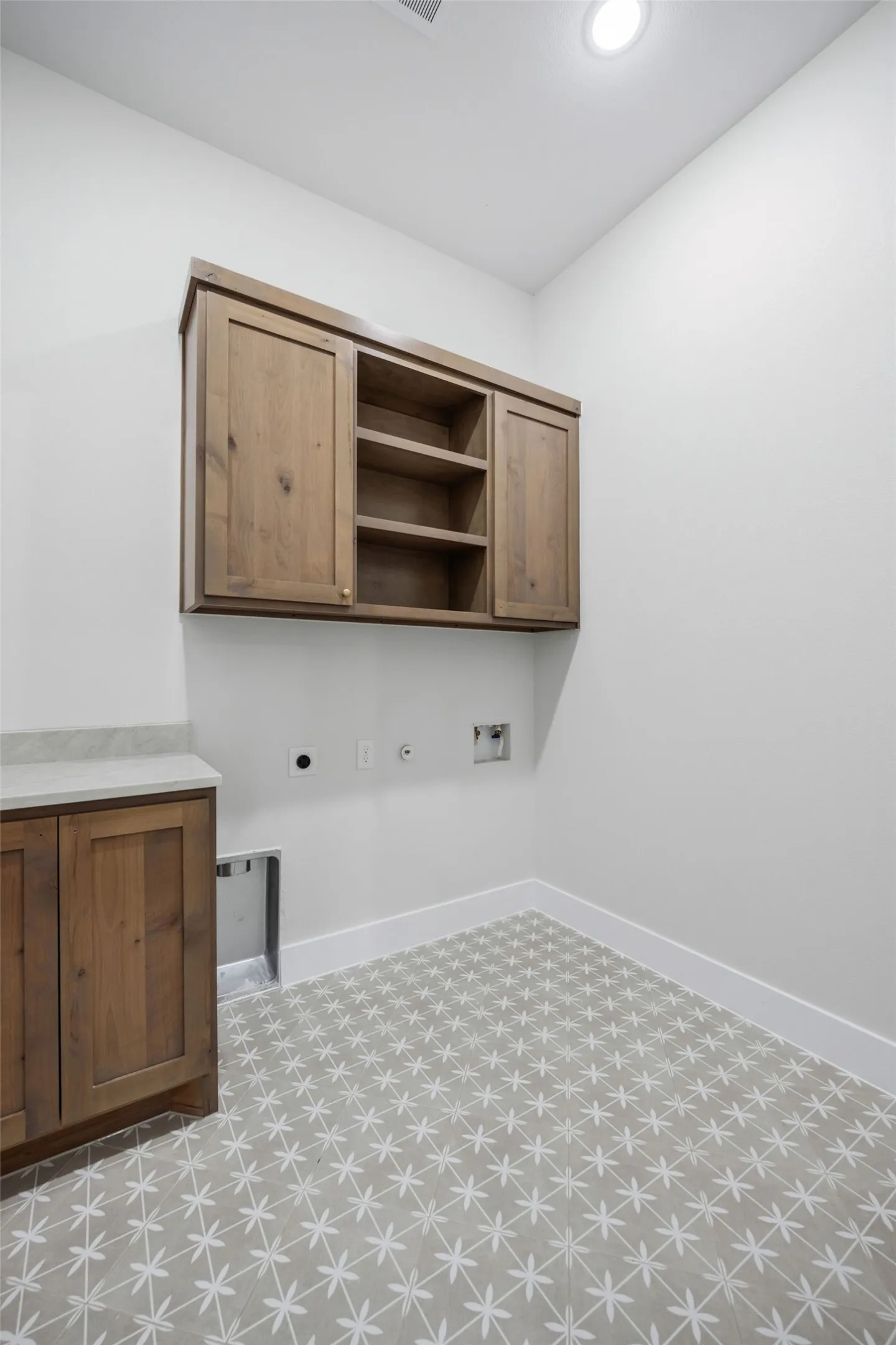Patterned floor tile, recessed lighting, wood-finish cabinetry, and a light-toned countertop