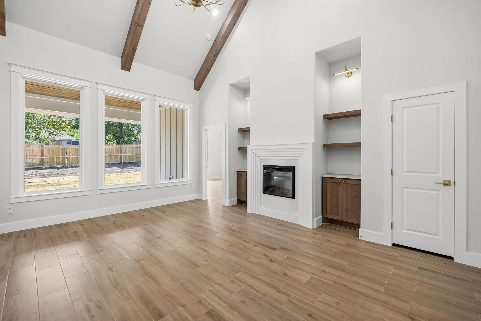 Vaulted ceiling with exposed wood beams, wood-finish flooring, built-in fireplace, built-in shelving, and multiple windows