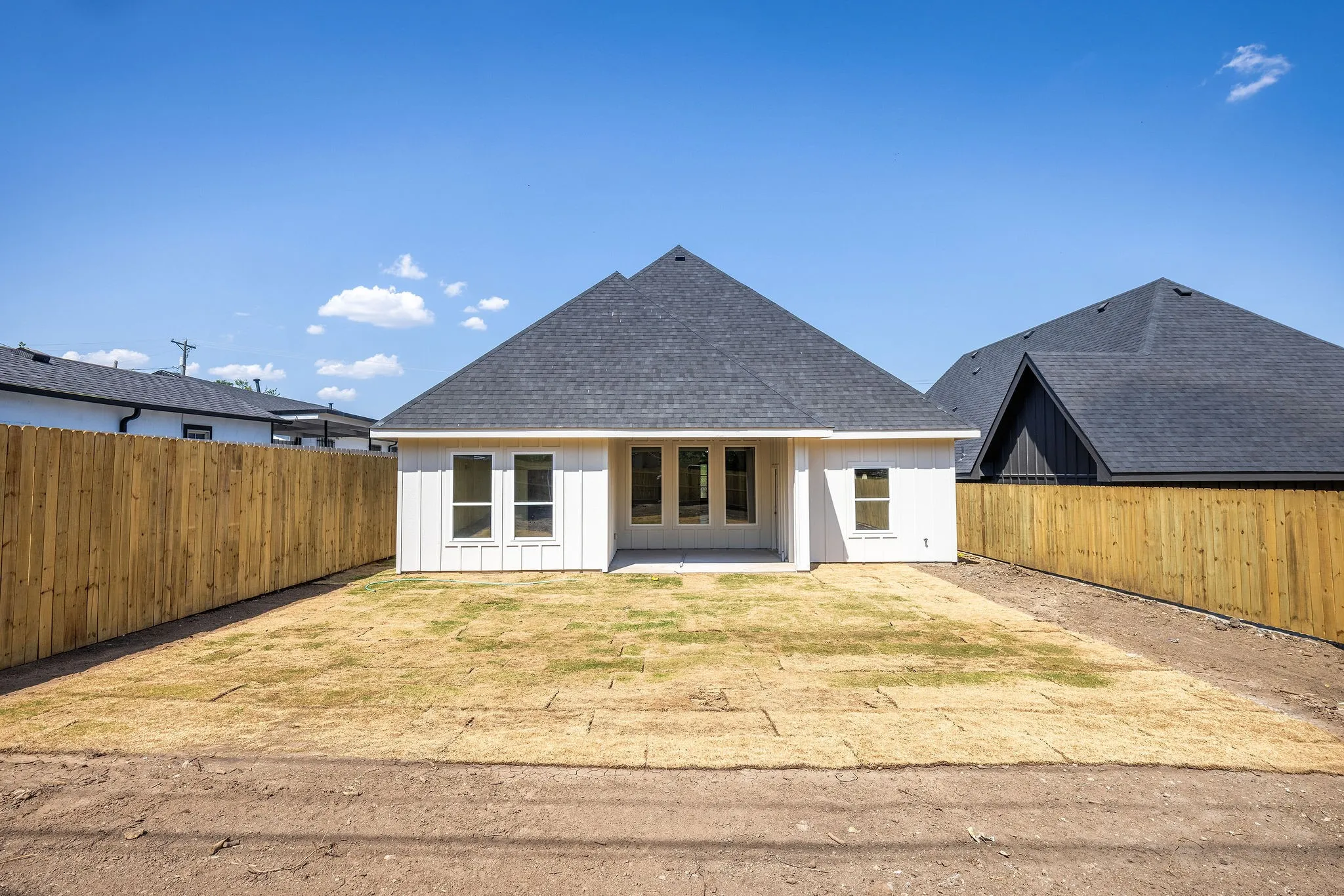 Rear exterior featuring white siding, a dark shingle roof, a concrete patio, and a wood privacy fence